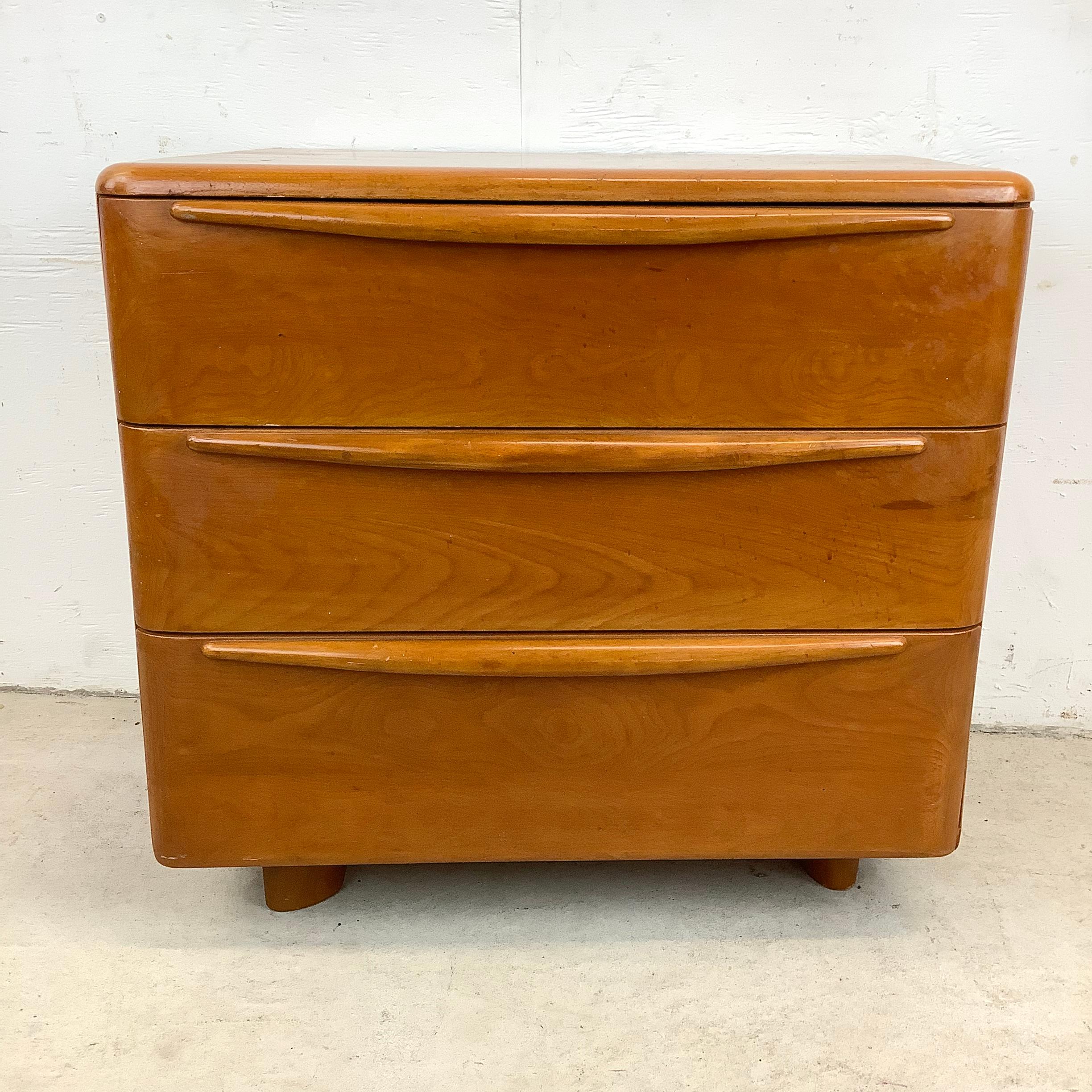 Introducing a timeless piece of mid-century craftsmanship: a three-drawer maple chest of drawers by the renowned Heywood-Wakefield, finished in their signature wheat finish. This versatile chest, perfect as a bedside nightstand, embodies both style