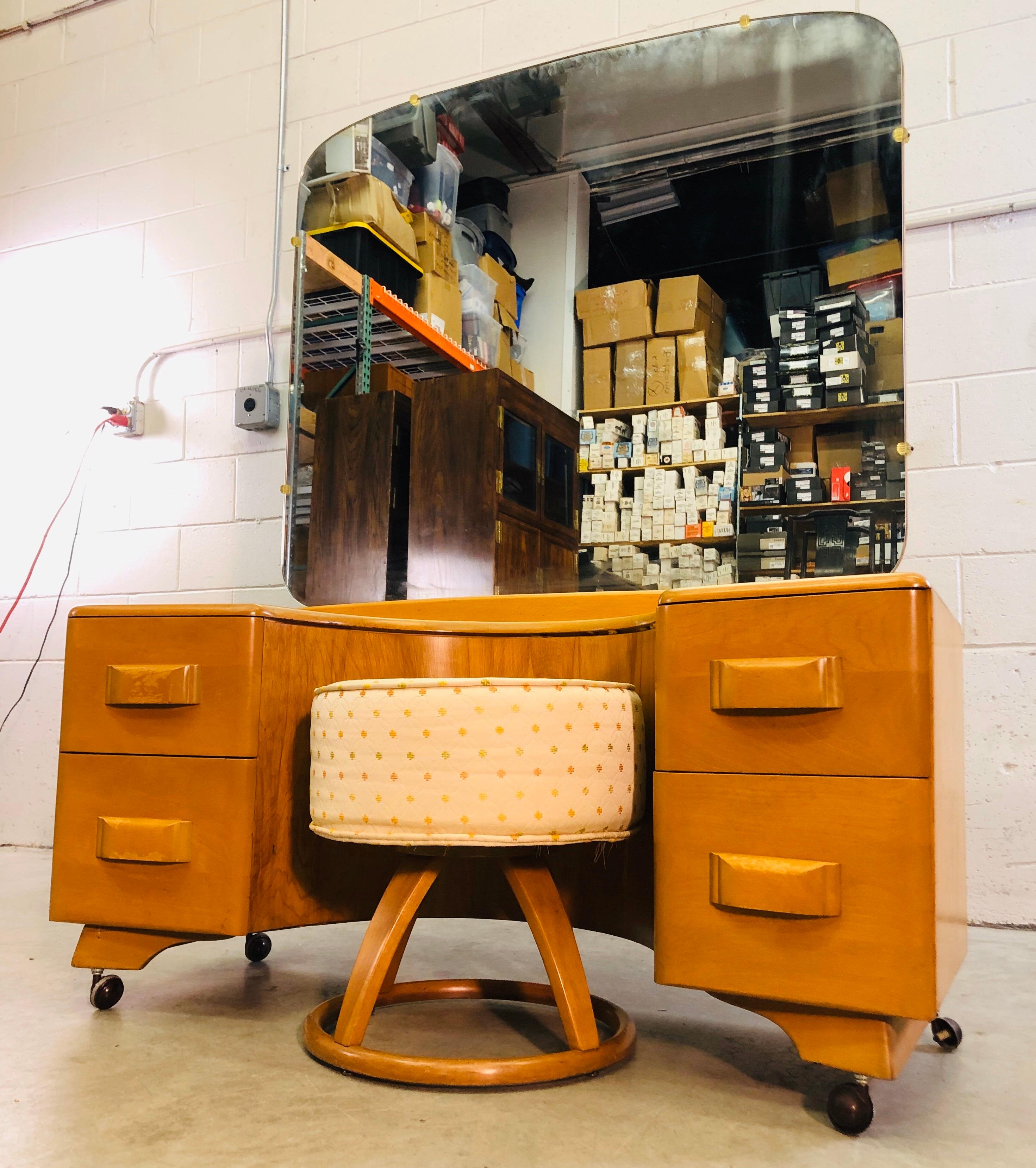 Vintage 1950s Heywood Wakefield maple wood vanity with mirror and foot stool set in the champagne finish. The vanity has 4 drawers for storage and comes with matching foot stool. Mirror is in excellent condition. Stool measures 18” diameter x 19”