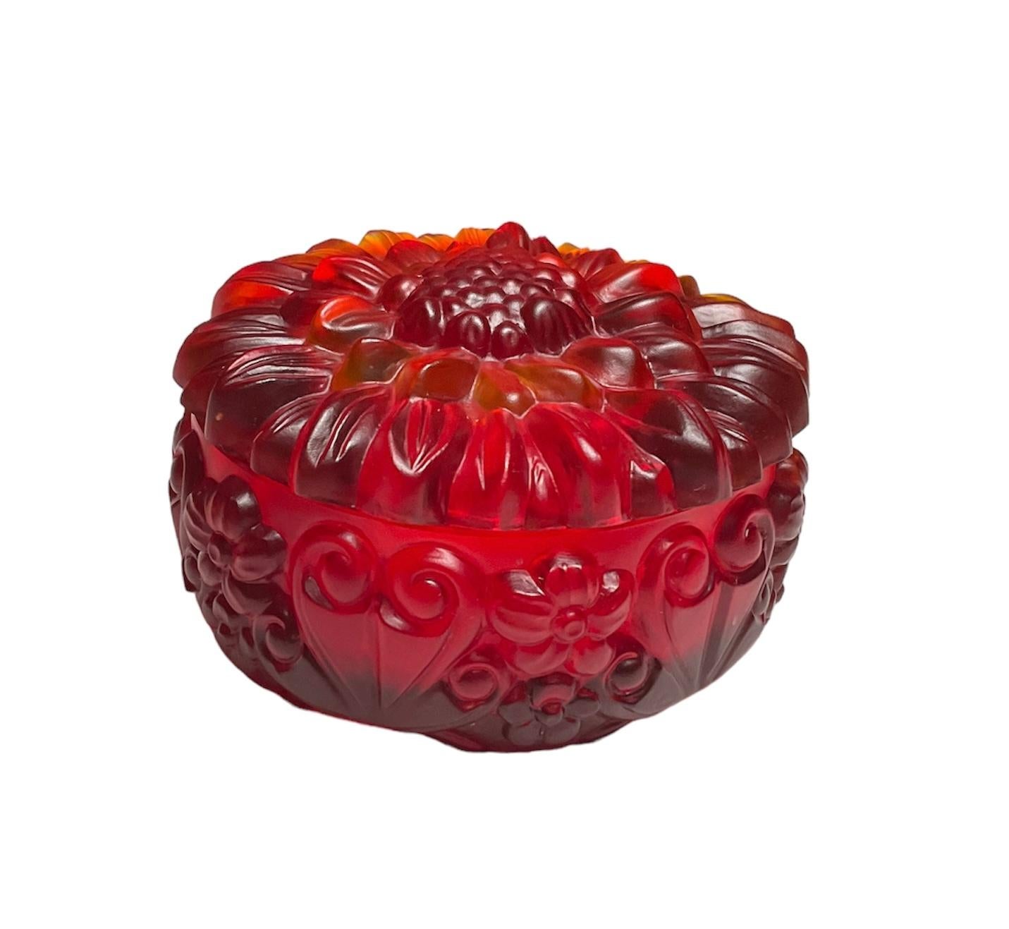 This is a H.Hoffman Red Glass Round Powder, Jewelry or Vanity Lidded Box. It depicts a round bowl decorated with a relief pattern of flowers and hearts. Also, the lid is adorned with a relief of a large peony like flower.