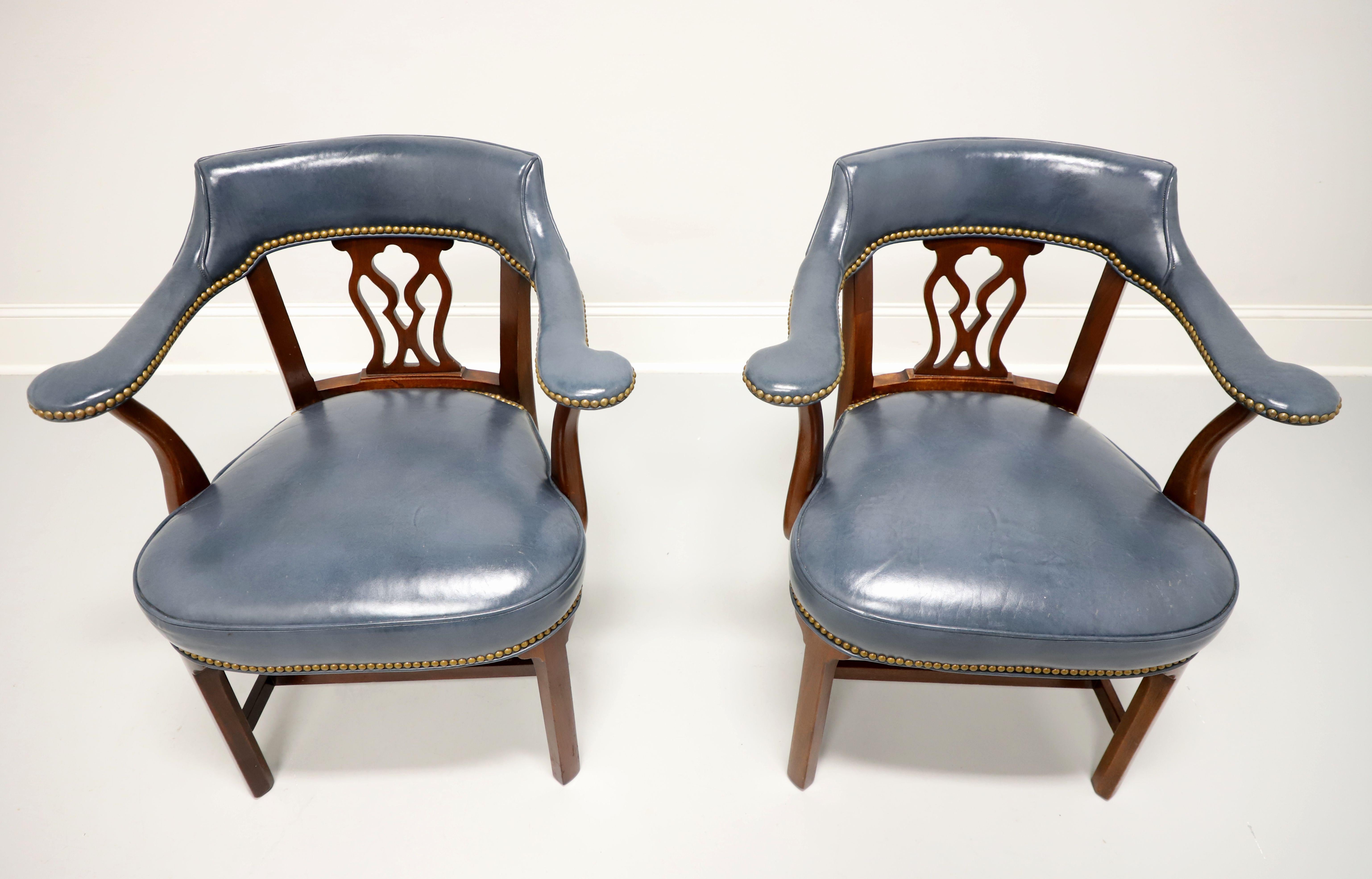 A pair of Traditional style armchairs by Hickory Chair. Mahogany frame with a decoratively carved backrest, blue color leather upholstered, barrel back, leather arms, brass nailhead trim, flared rear legs, carved straight front legs, and stretchers.