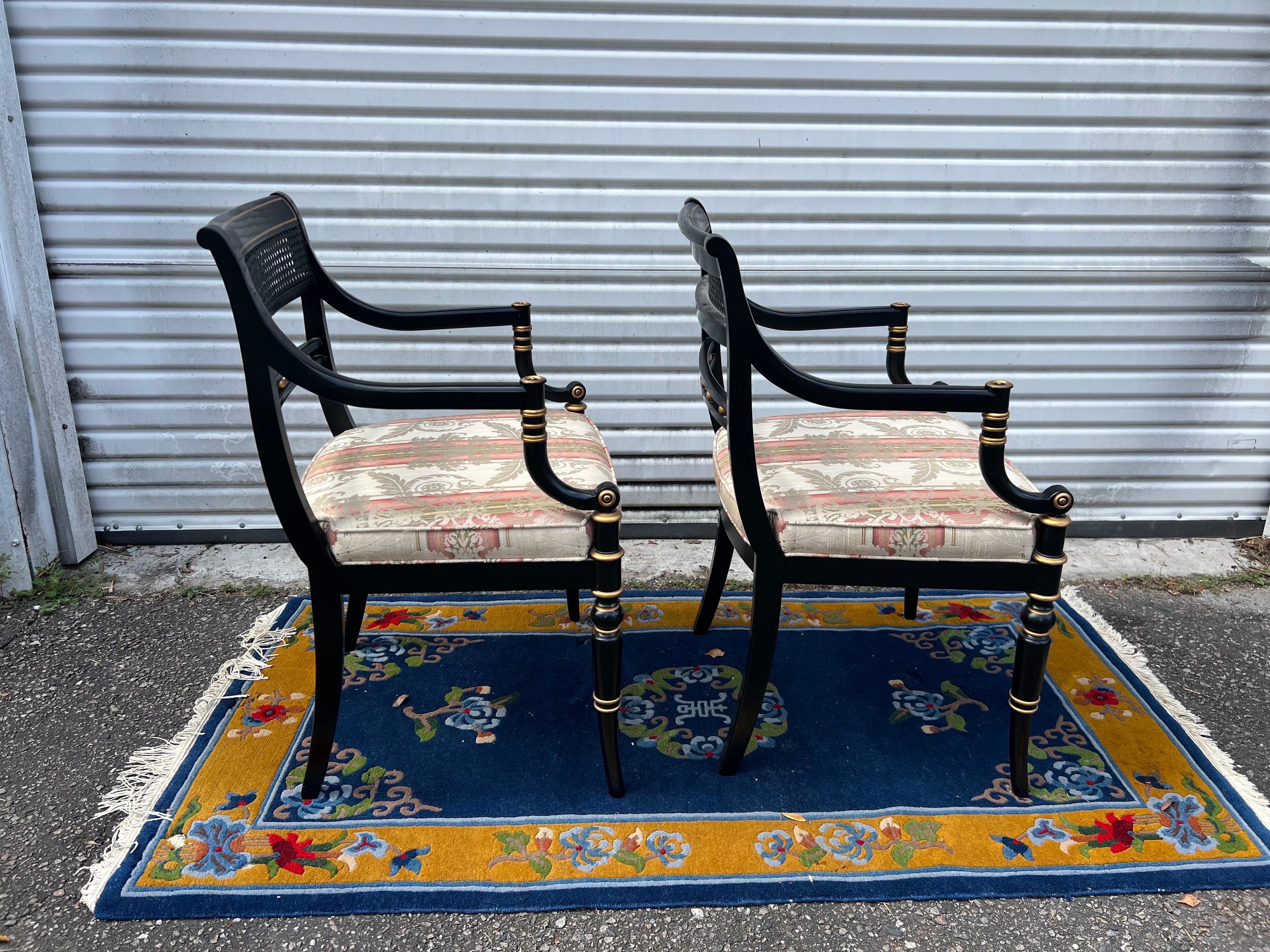 This set of elegant side chairs by Hickory Chair showcase an austere neoclassical styling and have been treated with a black and gold finish for decadent visual appeal. Inset cane panels decorate each chair’s squared back before leading into lithe