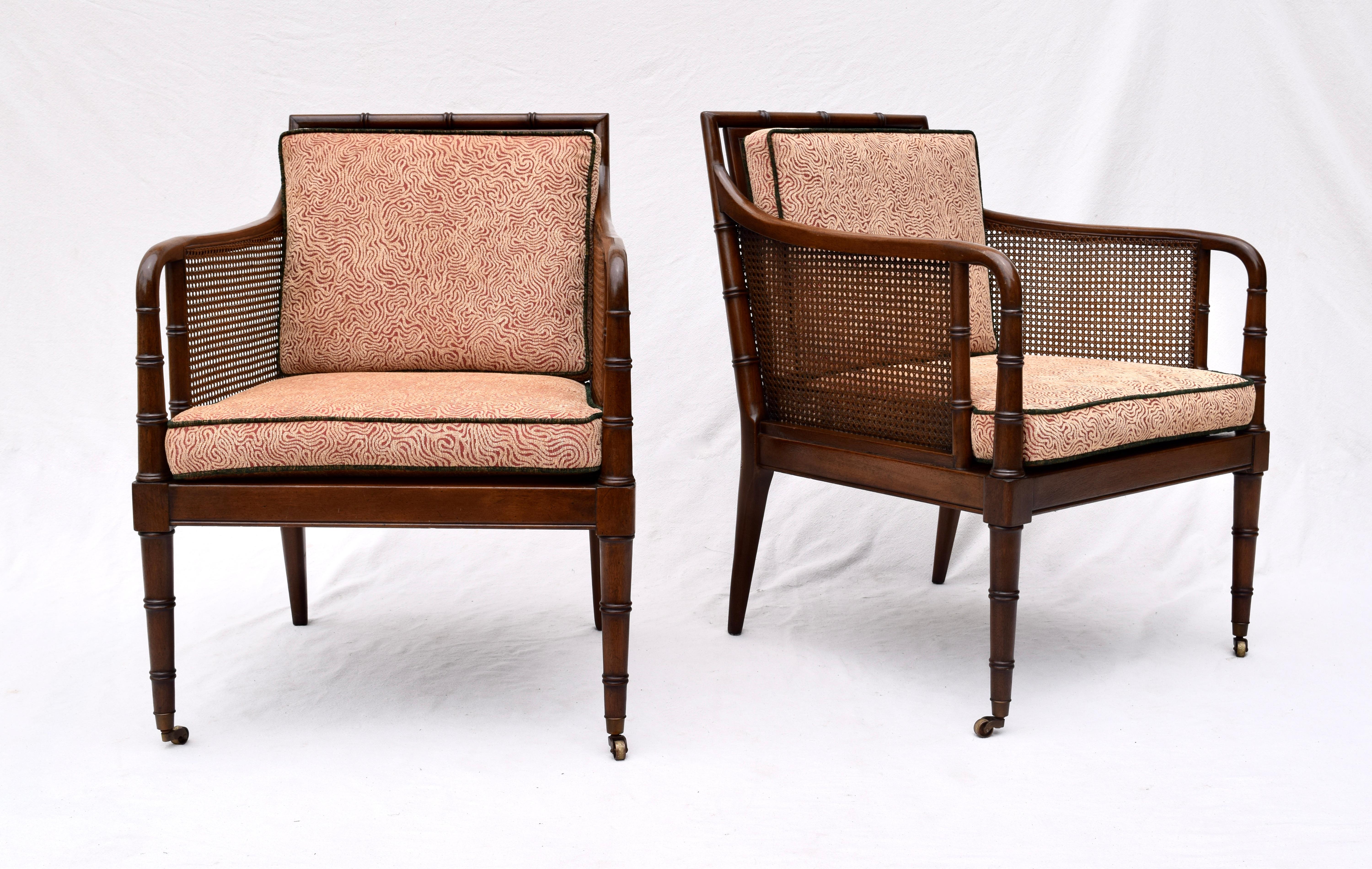 A pair of caned, faux bamboo Mahogany club, lounge or occasional chairs on brass casters. Beautifully maintained, the pair has been fully detailed and reupholstered. Caning is immaculate. Removable upholstered and fitted insert decks for support