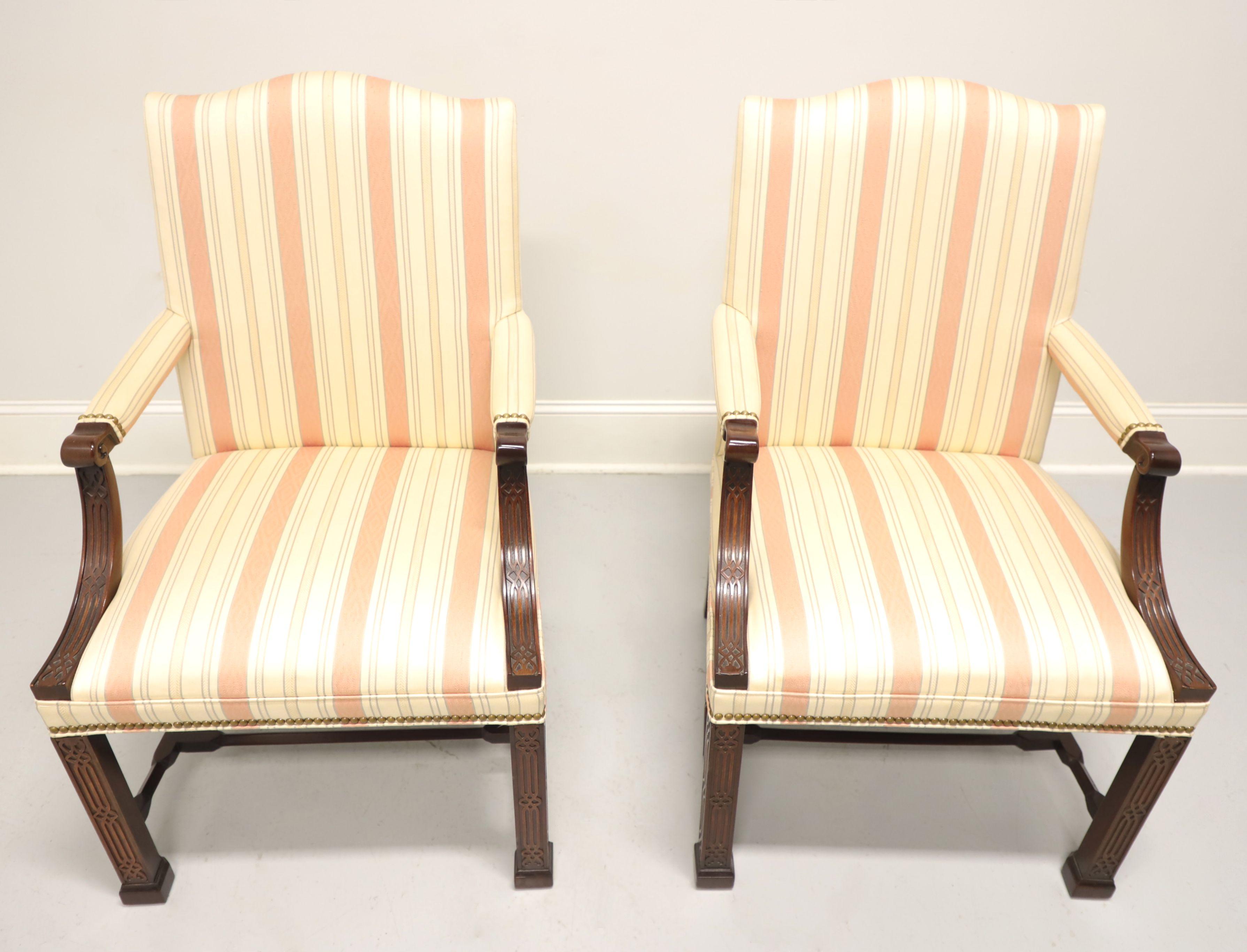 A pair of Chippendale style upholstered armchairs by Hickory Chair, their Wentworth. Mahogany frame, a neutral soft pink & beige color striped pattern fabric upholstery, upholstered arms with fretwork carved mahogany supports, brass nailhead trim,