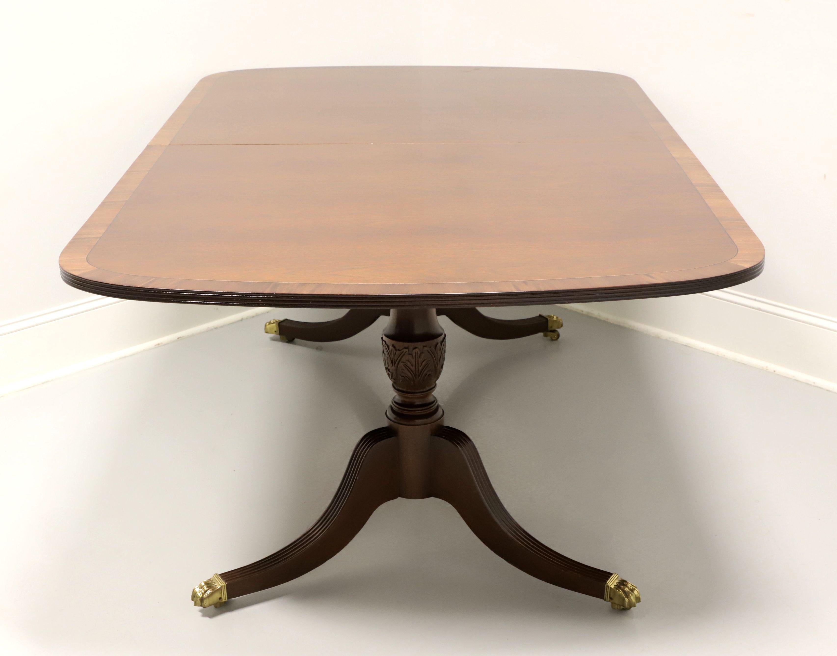 A Traditional style double pedestal dining banquet table by Hickory White. Mahogany with banding to top, ribbed edge, carved double pedestals with three fluted legs, brass paw toe caps and casters. Includes three 20 inch extension leaves for