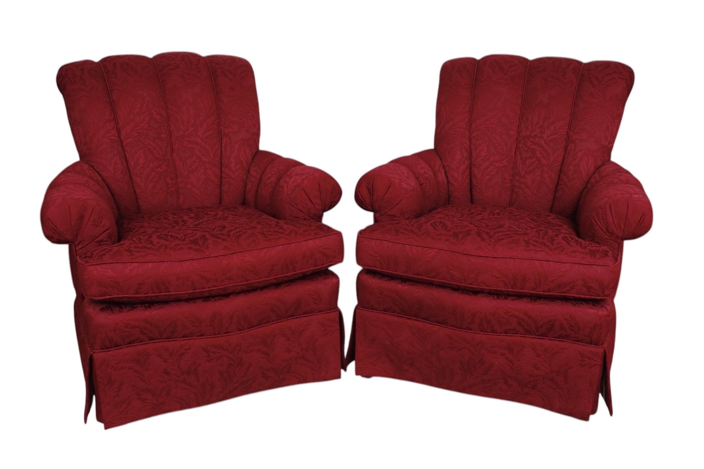 A pair of upholstered lounge chairs made by Hickory White of North Carolina. Reclining channel backs and channeled pleated arms frame thick cushioned seats. Skirts with kick pleated corners cover wooden legs. Upholstered throughout in a rich red