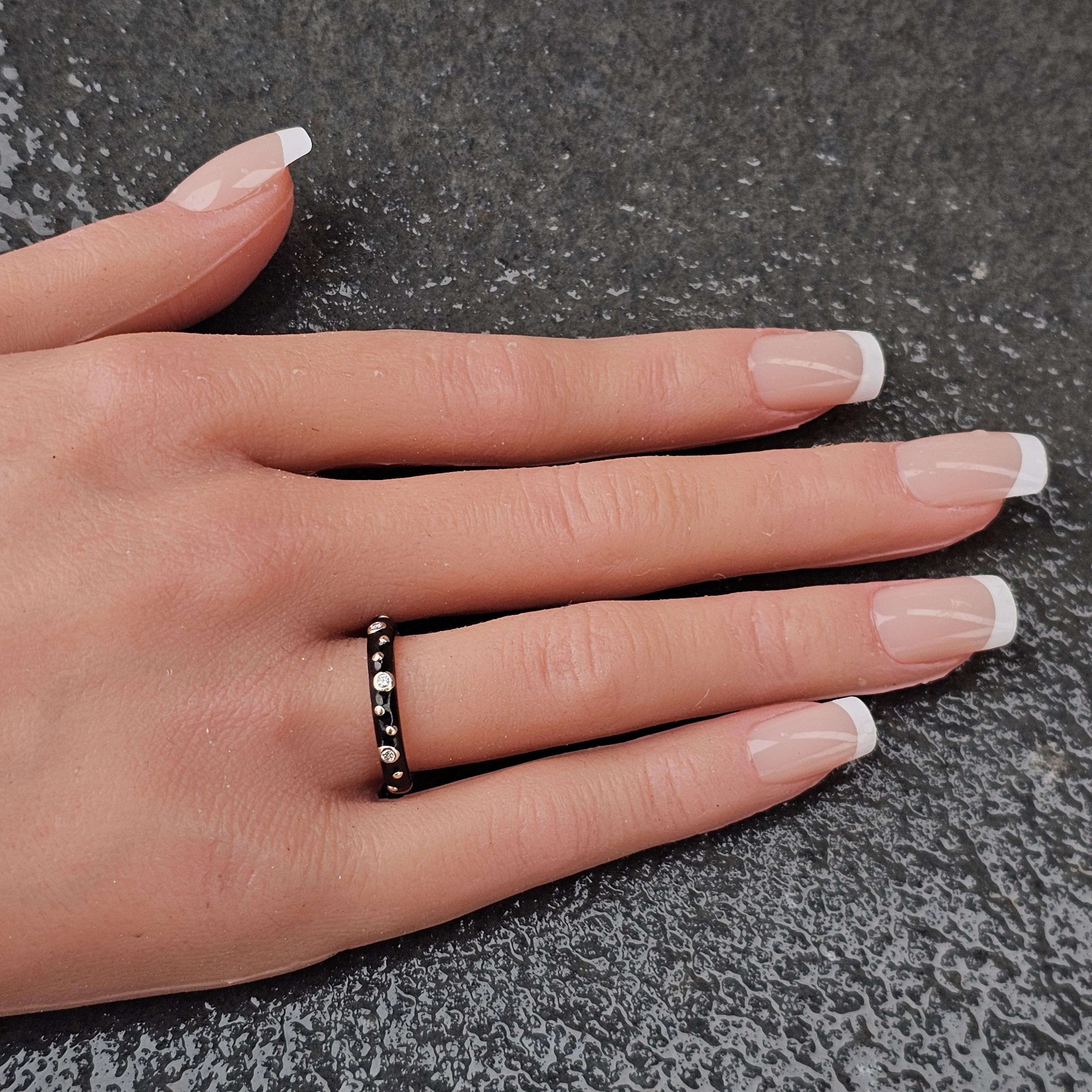 This Hidalgo band ring is a captivating piece of fine jewelry. The sleek design features a black enamel band with three round white diamonds, each set in 18k white gold bezels. The diamonds are evenly spaced, creating a striking contrast against the