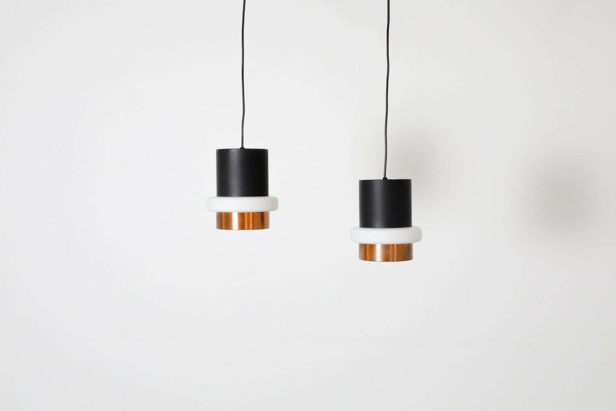 Cylindrical in form, a thick milk glass ring seperates the enameled black upper portion of the light from the lower copper portion. Classic Dutch Mid-Century light designed by Hiemstra Evolux. These pendants use a standard size medium base bulb. No