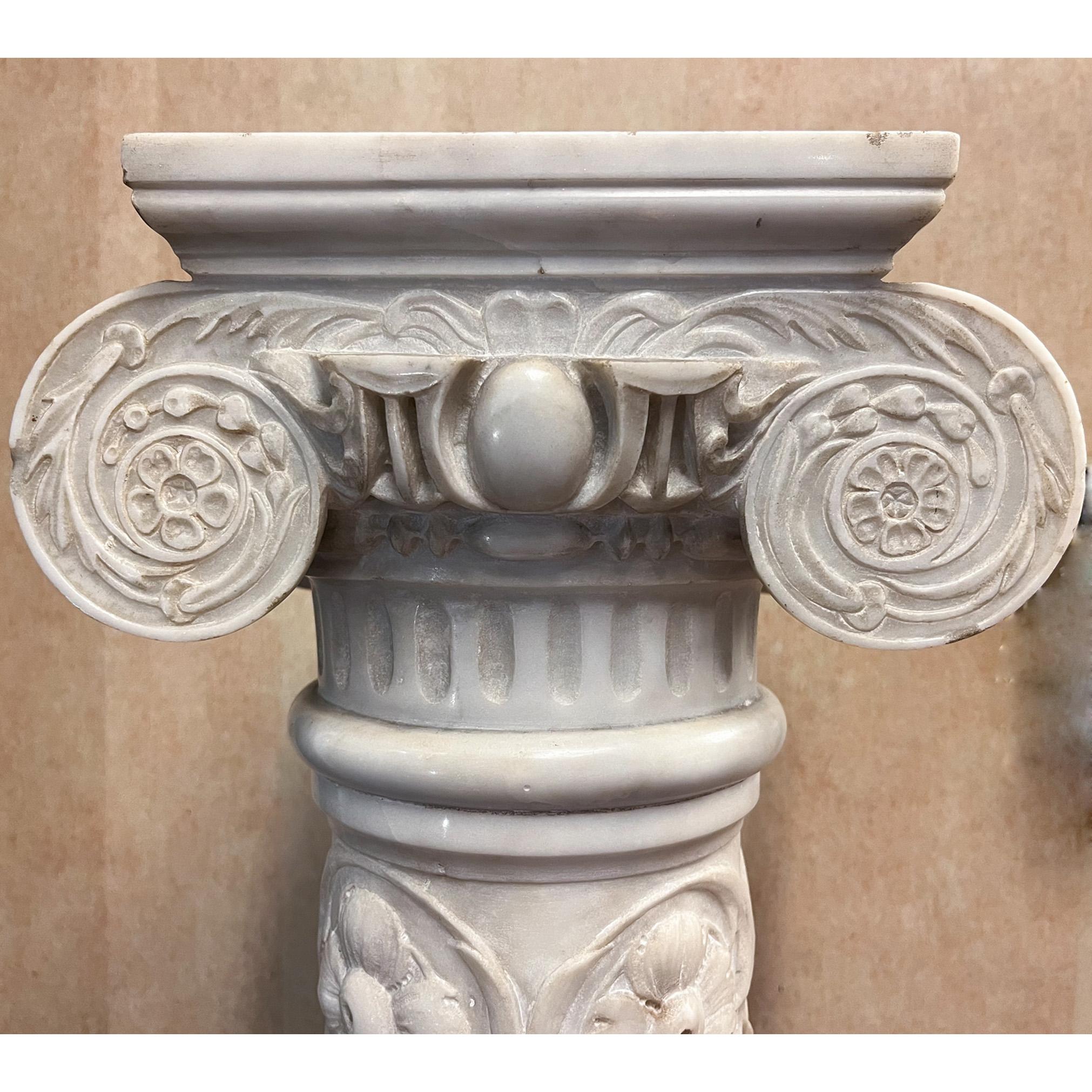 Tall Ionic column pedestal made of white marble with carved high relief garlands and low relief floral, foliage and mythical animal details. Square crown and base with scroll capital, shaft reliefs done utilizing a reflective design motif throughout