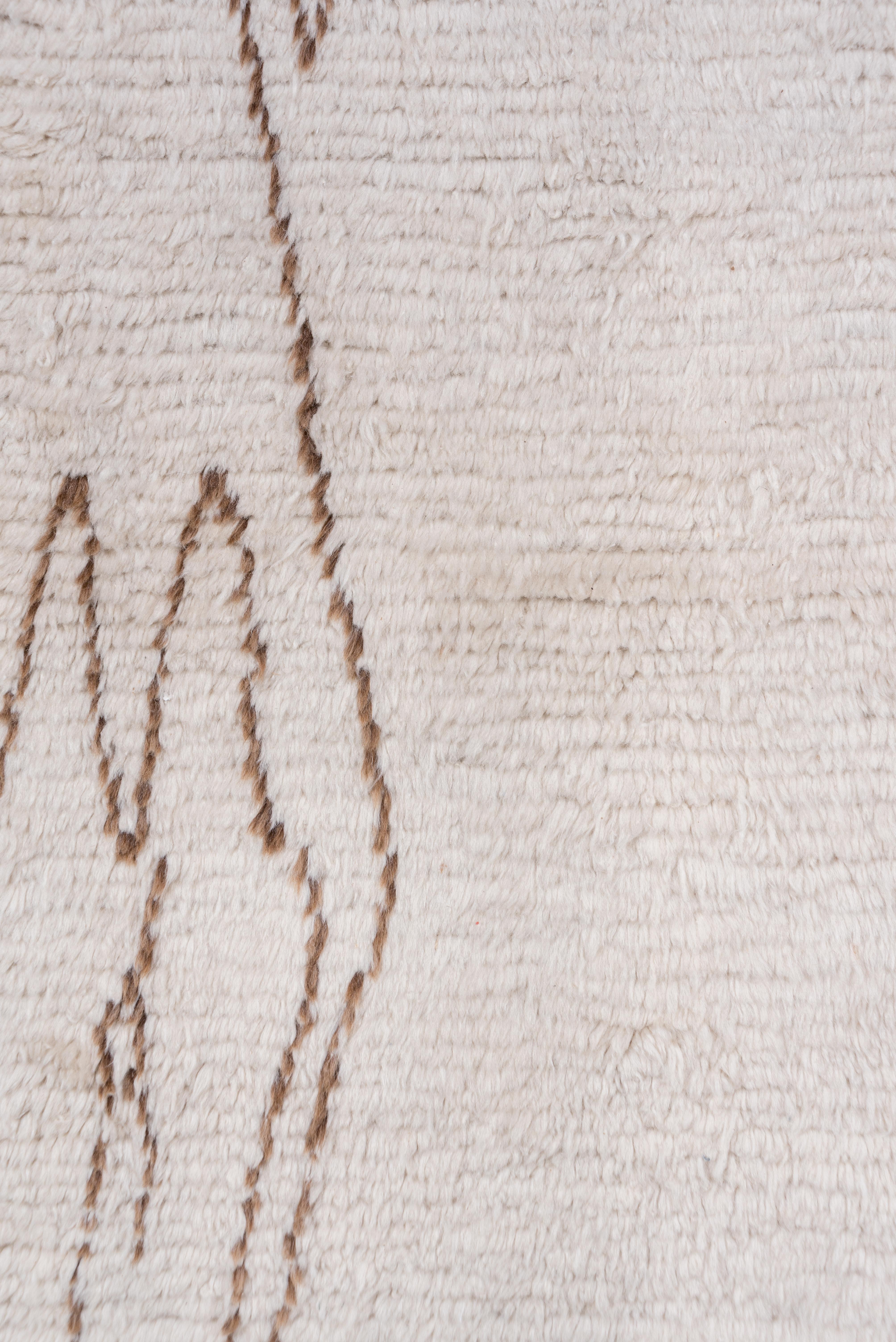 This borderless High Atlas runner has a medium-long recumbent pile in creamy ivory undyed wool and a geometric pattern in medium brown of tall, conjoint lozenges, and various tall open motives scattered irregularly with much of the center open and