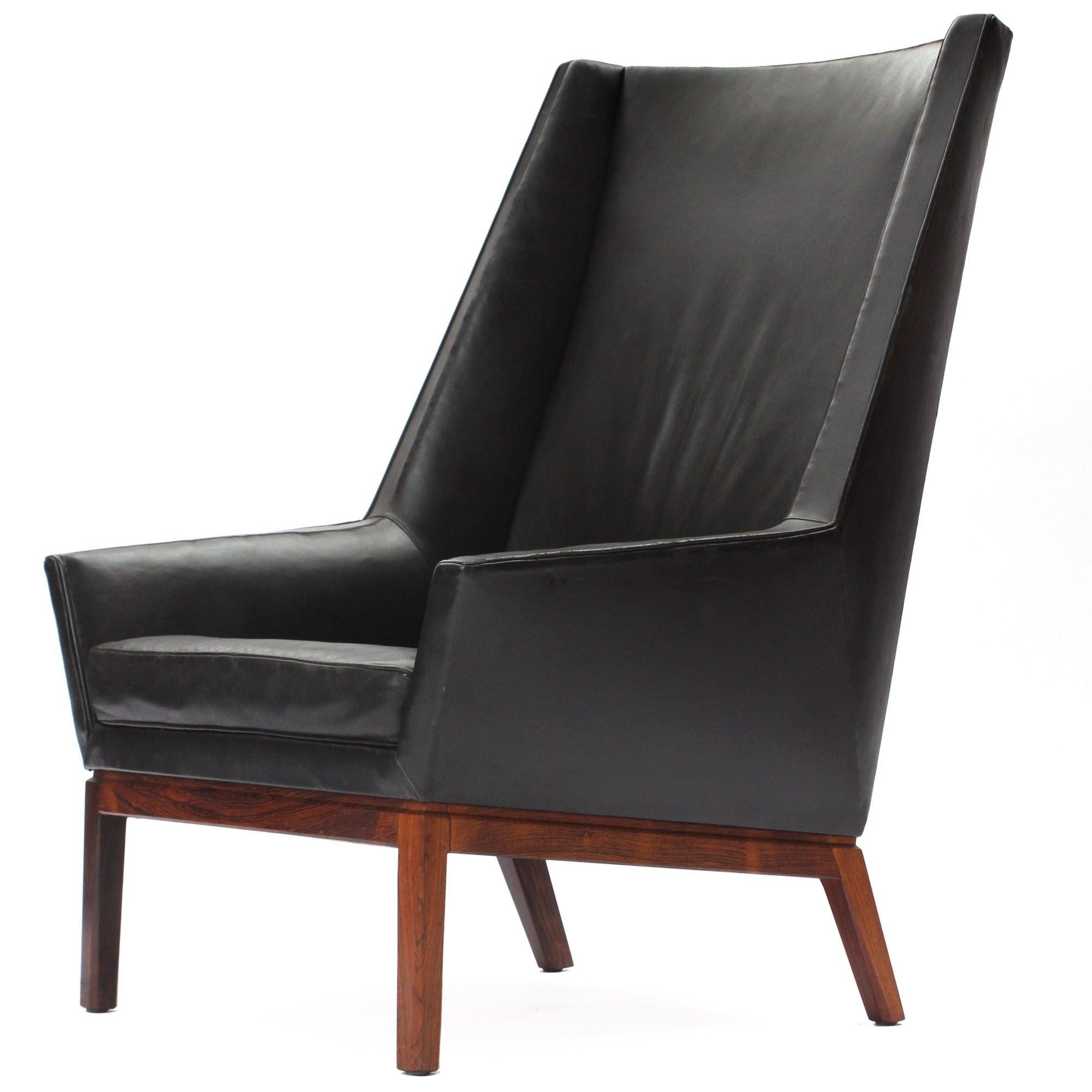 Sillón de respaldo alto con tapicería original de cuero negro y armazón de palisandro.