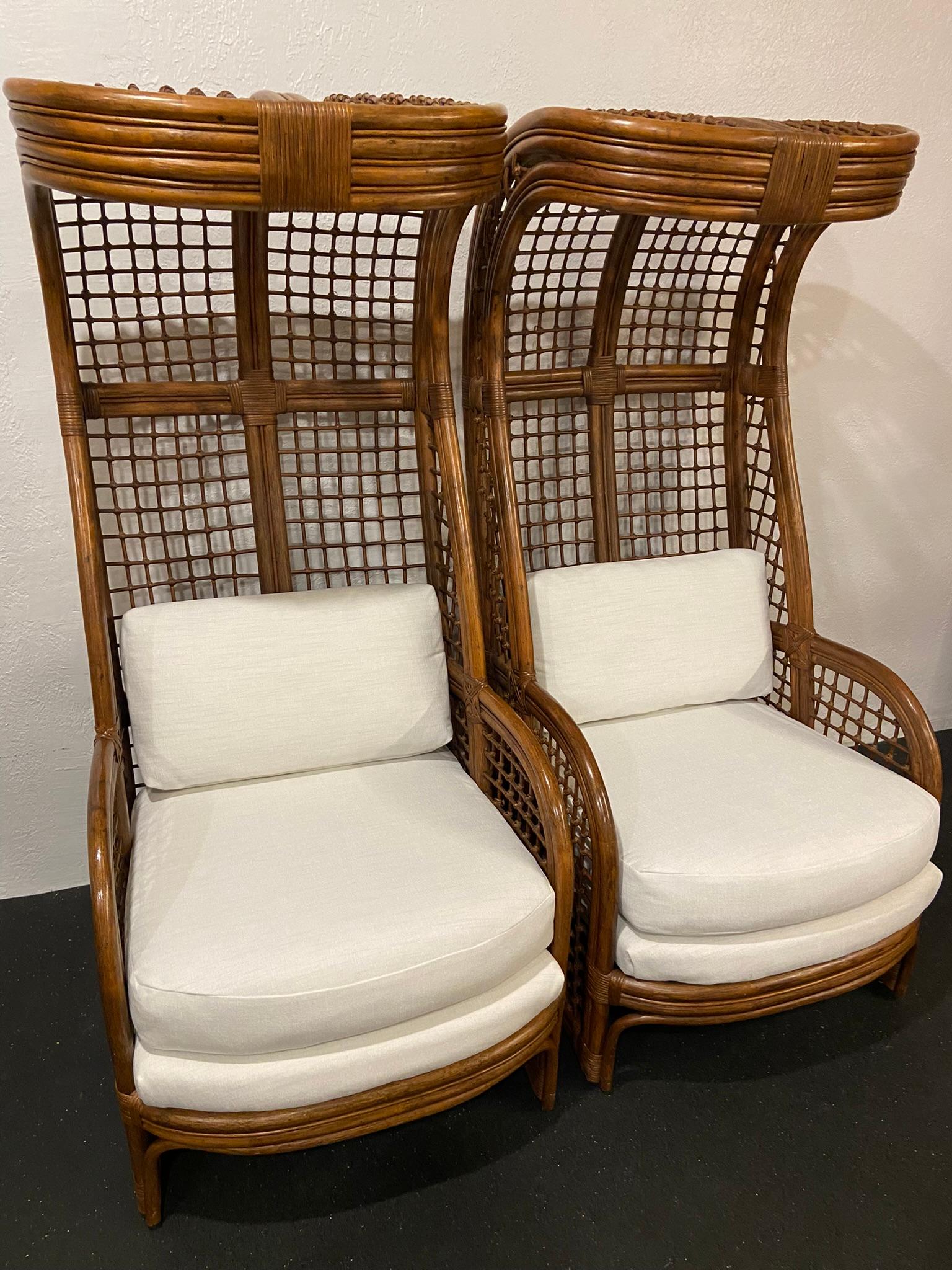Pair of high back hooded rattan lounge chairs. Dramatic scale in extremely rare form. Newly upholstered in a chenille/velvet blend. Small areas of cane wrap that has loosened and old cane repair (please refer to photos).

Would work well in a