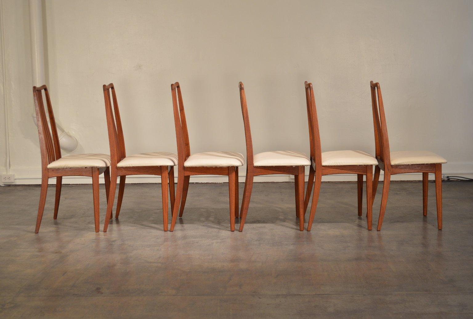 A set of six high-back teak dining chairs designed by Anders Jensen for Holstebro of Denmark. The solid teak backs have sculptural tops and the slats have a gentle s-curve.

White vinyl seat upholstery. All six chairs have original translucent