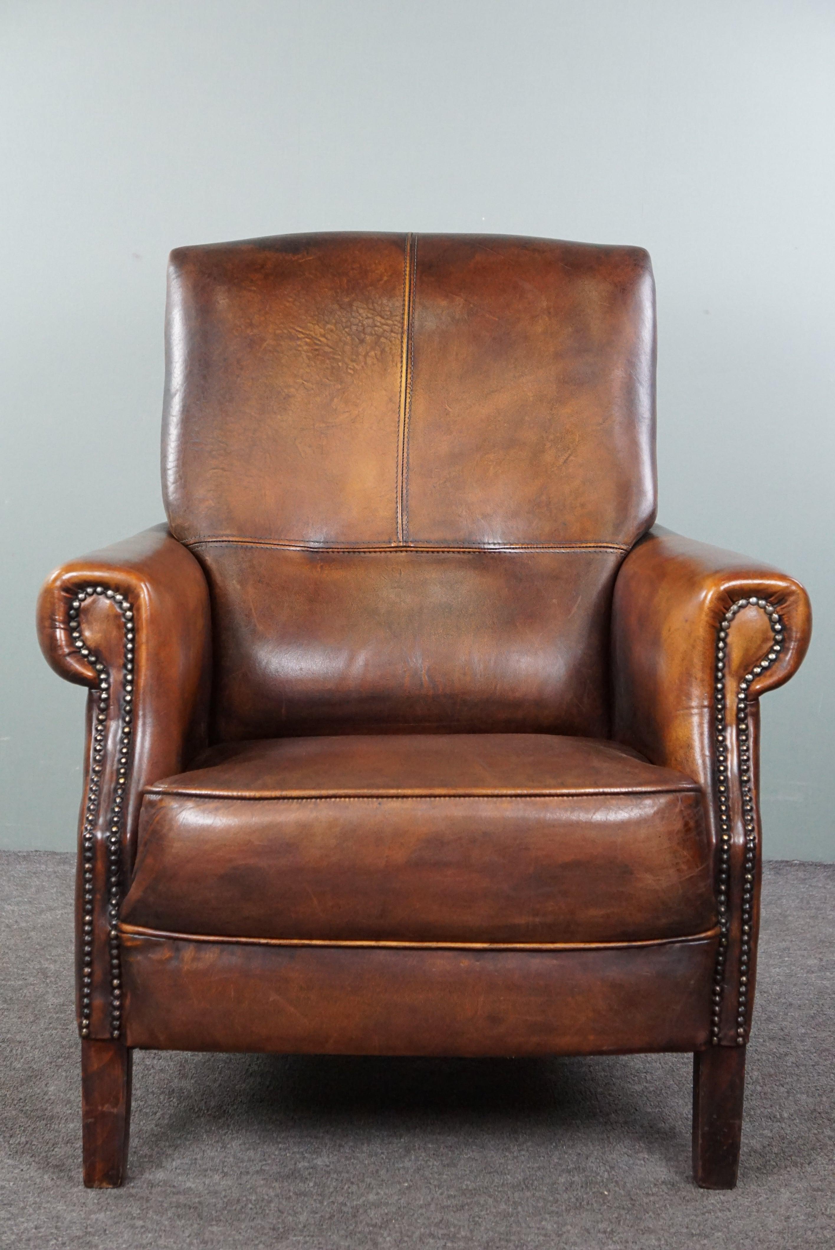 Offered is this beautiful sheep leather armchair with a fantastic appearance. This lovely armchair, in good condition, not only boasts stunning colors but also offers a delightfully comfortable seat. With its classic nail finish, this dignified