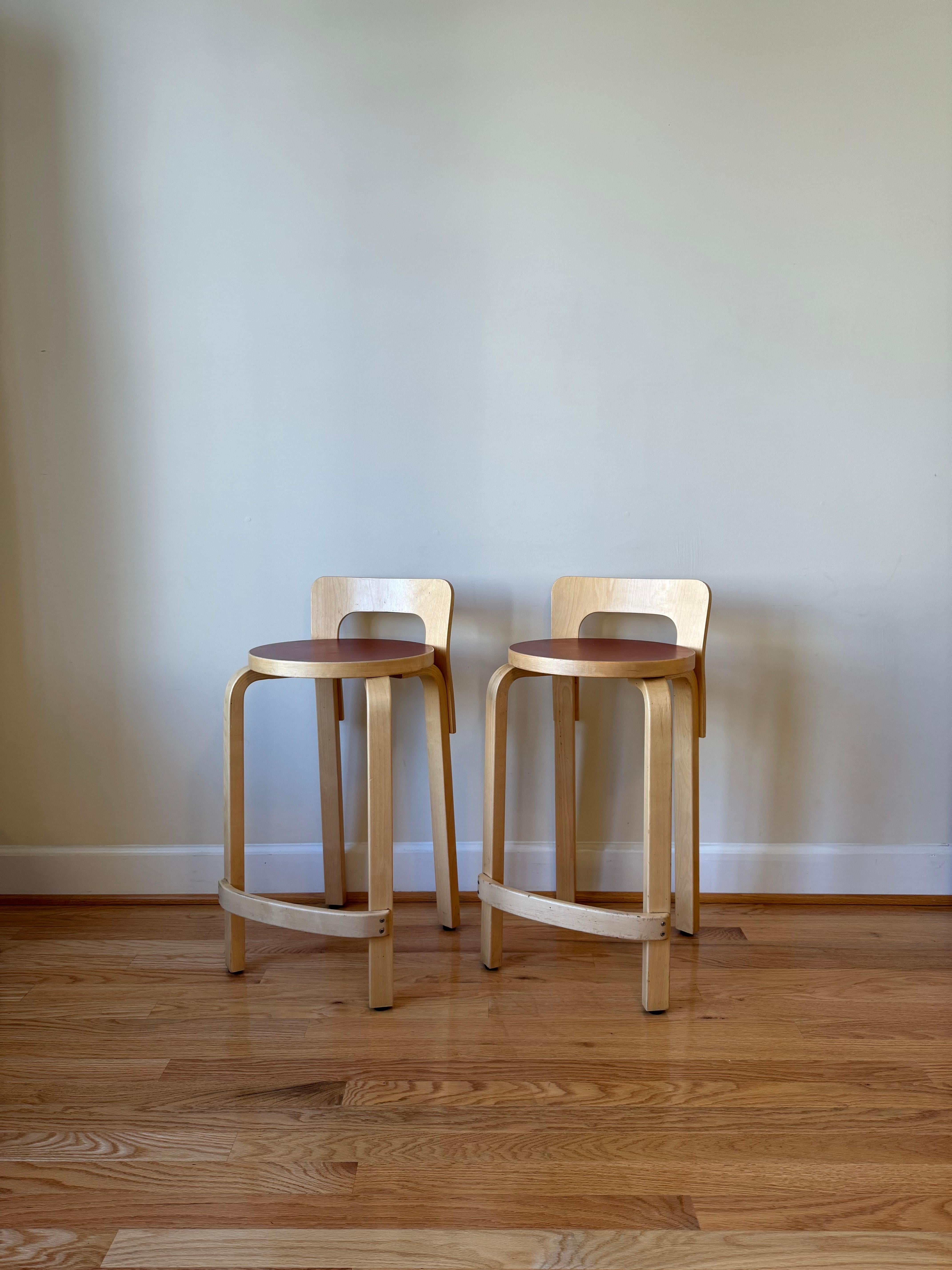 Der langbeinige High Chair K65 von Alvar Aalto hat die optimale Höhe für Stehtische und Bartresen. Die niedrige Rückenlehne bietet genau die richtige Unterstützung für den Rücken, und die gebogene Schiene dient als perfekte Fußstütze. 
Als Teil der