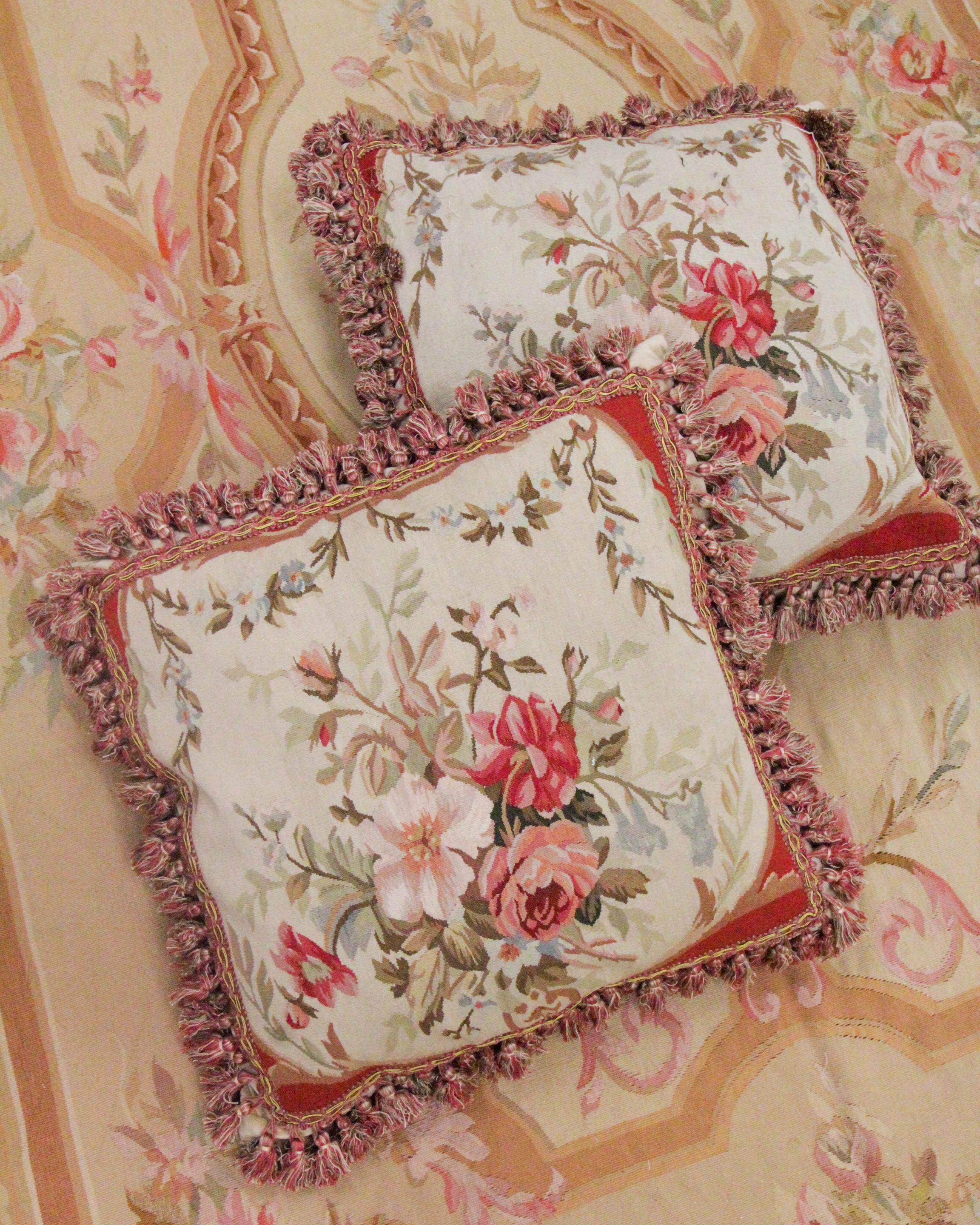 This elegant wool cushion cover is a beautiful accessory that has been delicately woven by hand with fine hand-spun wool and cotton. The central design reveals a graceful floral design with pink, red, brown, and green accents. The rug's edges have