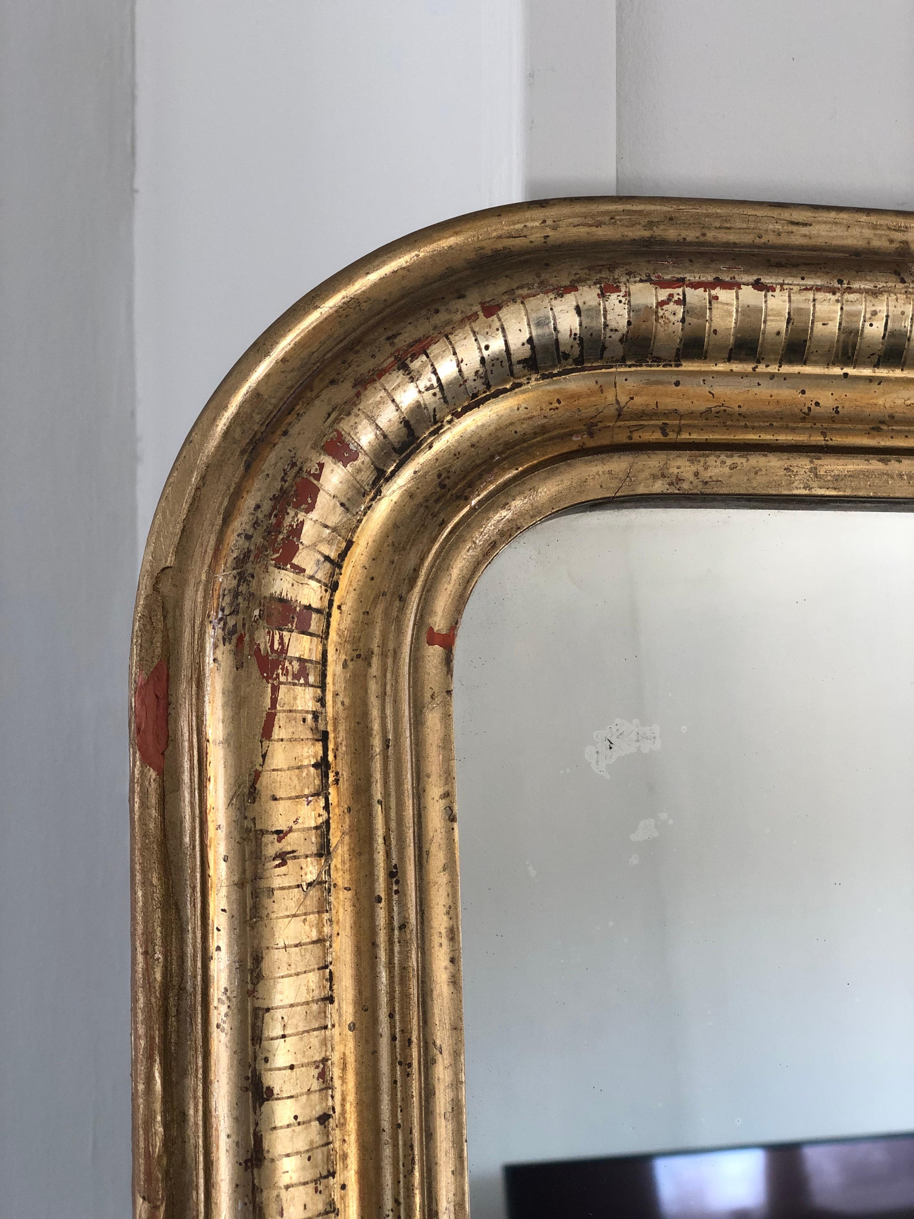 A very high-quality antique Louis Philippe mirror from France, late 19th century. An appearance with grandeur. The richly carved giltwood frame with curved top corners has a beautiful worn gold leaf patina. Original mercury glass and