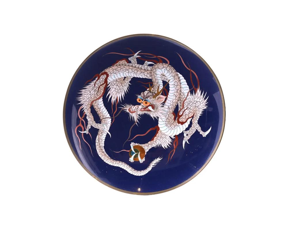 An antique Japanese Meiji era, enamel over copper charger plate. The plate is adorned with a polychrome image of a dragon on cobalt blue ground made in the Cloisonne technique. The backside is decorated with a swirl motif made in the Cloisonne