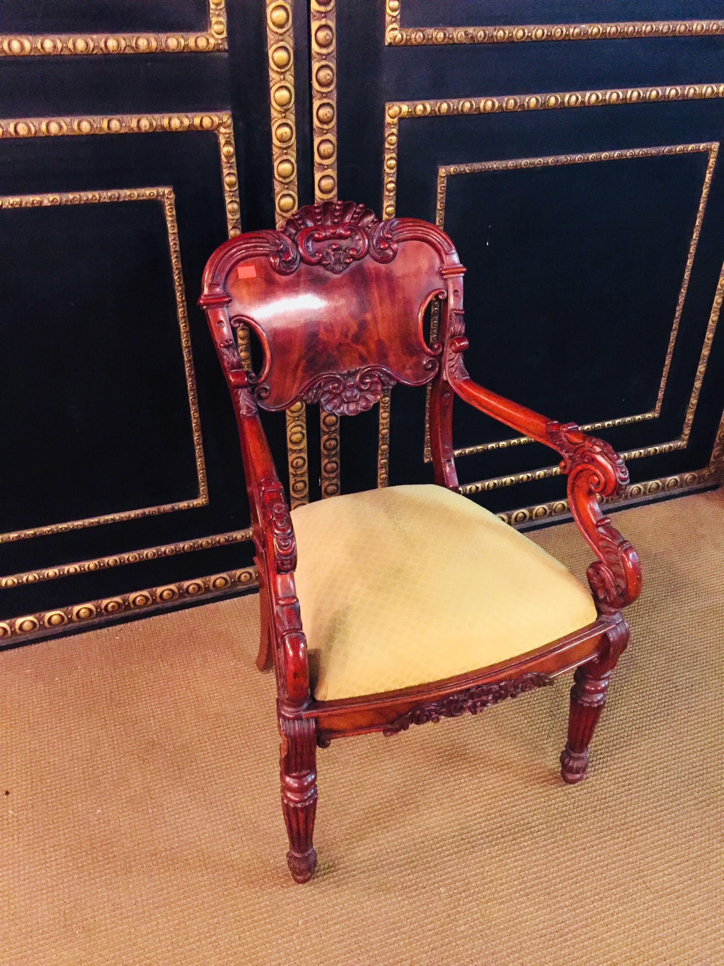 Solid mahogany. Curved frame on ballustrade legs with attached foliage. Strongly curved supports for slightly rising armrests. Rectangular, profiled, richly carved backrest frame with broad end crowned with sculpted Rocaillenbekrönung. Seat newly