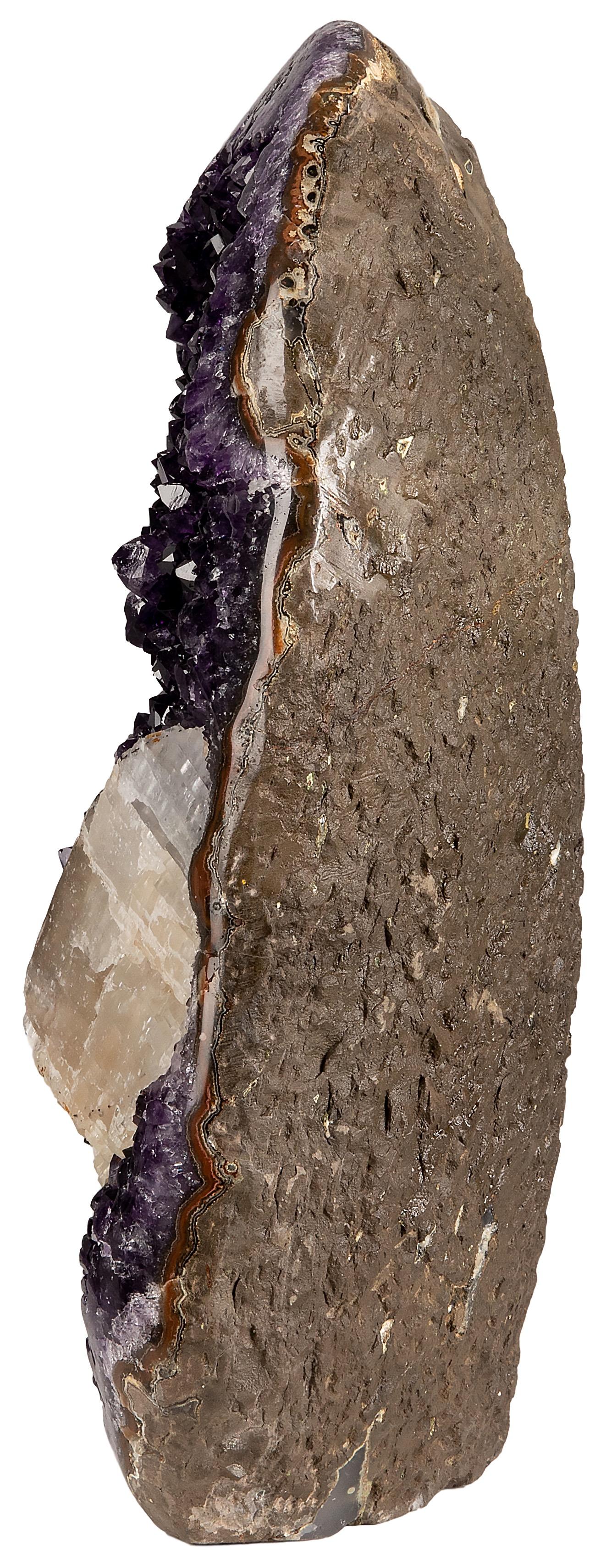 Une superbe améthyste d'un violet profond avec une formation de calcite. Du basalte brut à l'extérieur, aux cristaux d'améthyste violets de haute qualité à l'intérieur et à la formation de calcite, cette pièce présente une combinaison exquise de