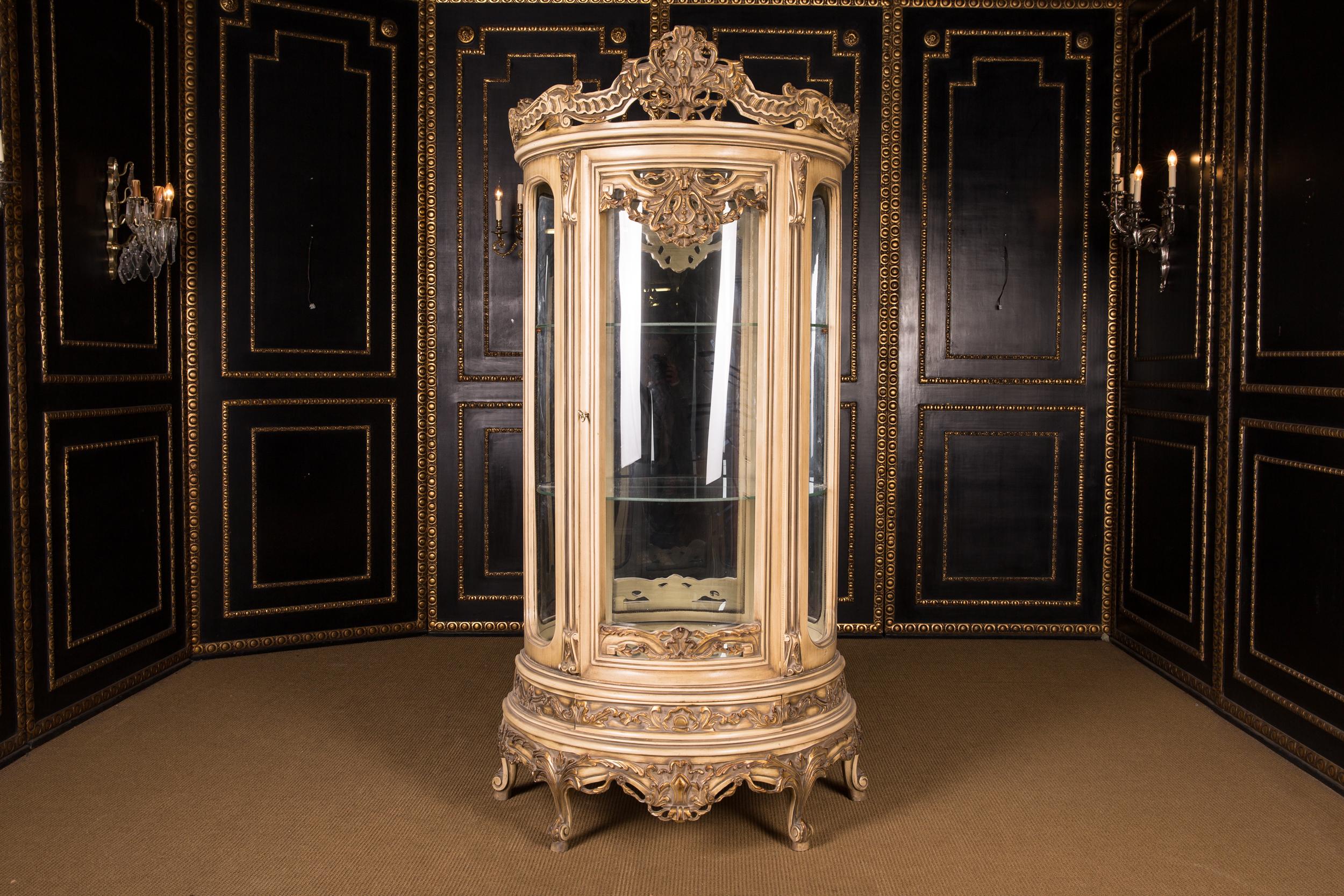 Massive, finely carved beech wood, colored and gilt gilded. High-rectangular, half-round and one-door cambered body, glazed from three sides. On curved feet one-door scalloped frame. Back wall mirrored three glass shelves. Carcass-shaped framing