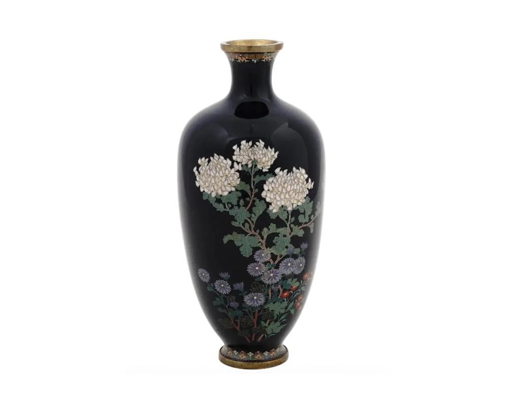 A high quality antique Japanese late Meiji period enamel over brass vase. The vase has an amphora shaped body and a fluted neck. The ware is enameled with a polychrome image of blossoming flowers on the black ground made in the Cloisonne technique.