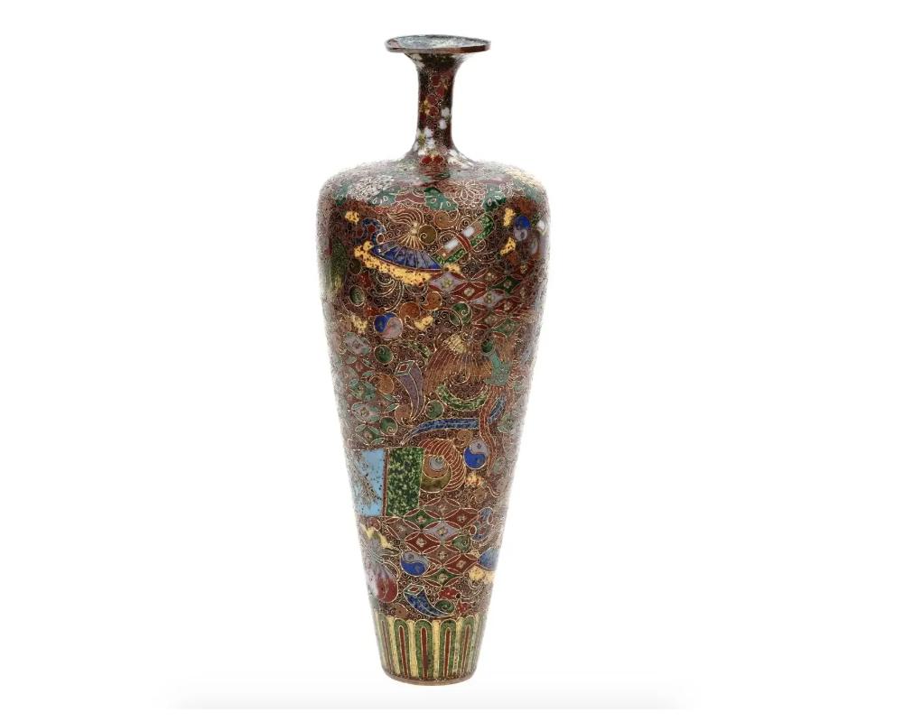 A high quality antique Japanese, late Meiji period, enamel over brass bud vase. The vase has an amphora shaped body and a narrow fluted neck. The ware is enameled with polychrome images of blossoming flowers, fans, traditional compositions,