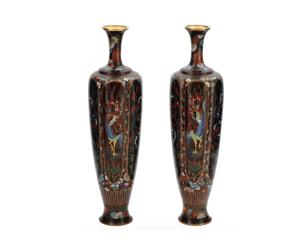A pair of high quality symmetrical Japanese, Meiji era, enamel over brass vases. Each vase has an amphora shaped body and a tall narrow neck. The ware is enameled with polychrome panels depicting Phoenix birds and dragons surrounded by floral and