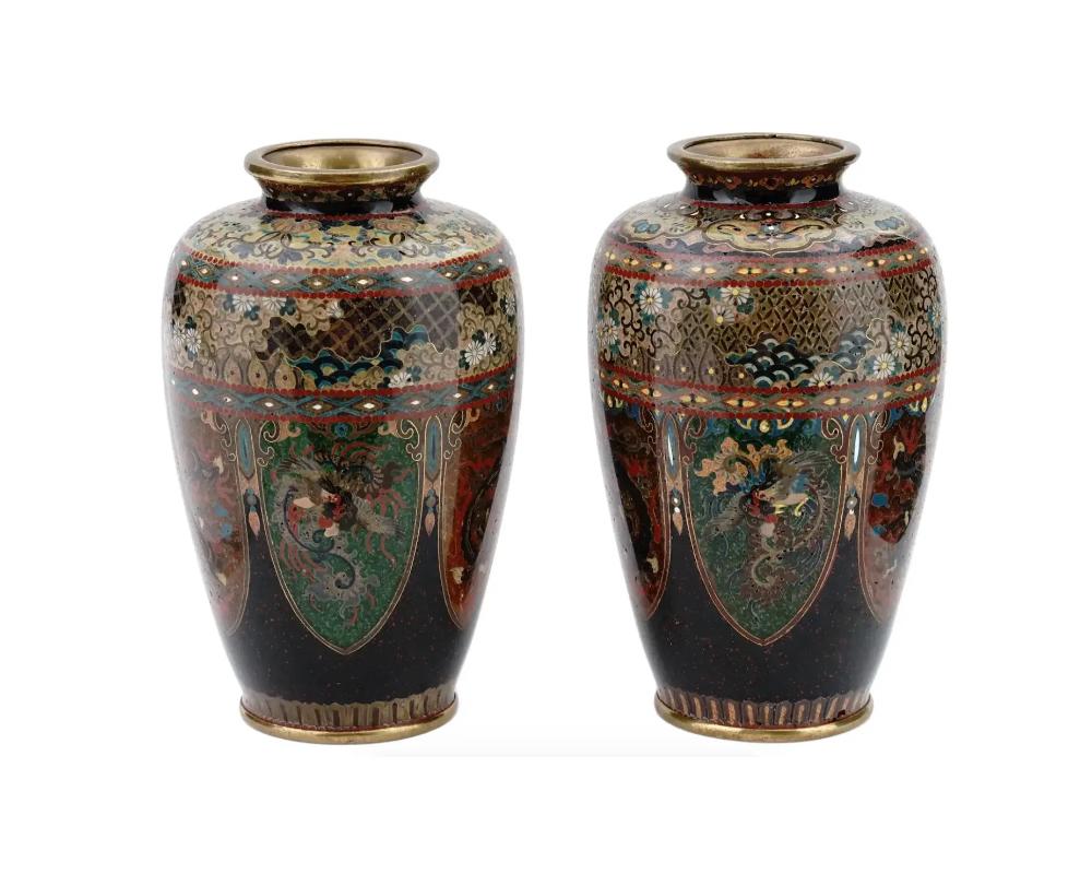 A pair of high quality symmetrical Japanese, Meiji era, enamel over brass vases. Each vase has an amphora shaped body and a short wide neck. Each ware is enameled with polychrome panels depicting Phoenix birds and dragons surrounded by a scrollwork