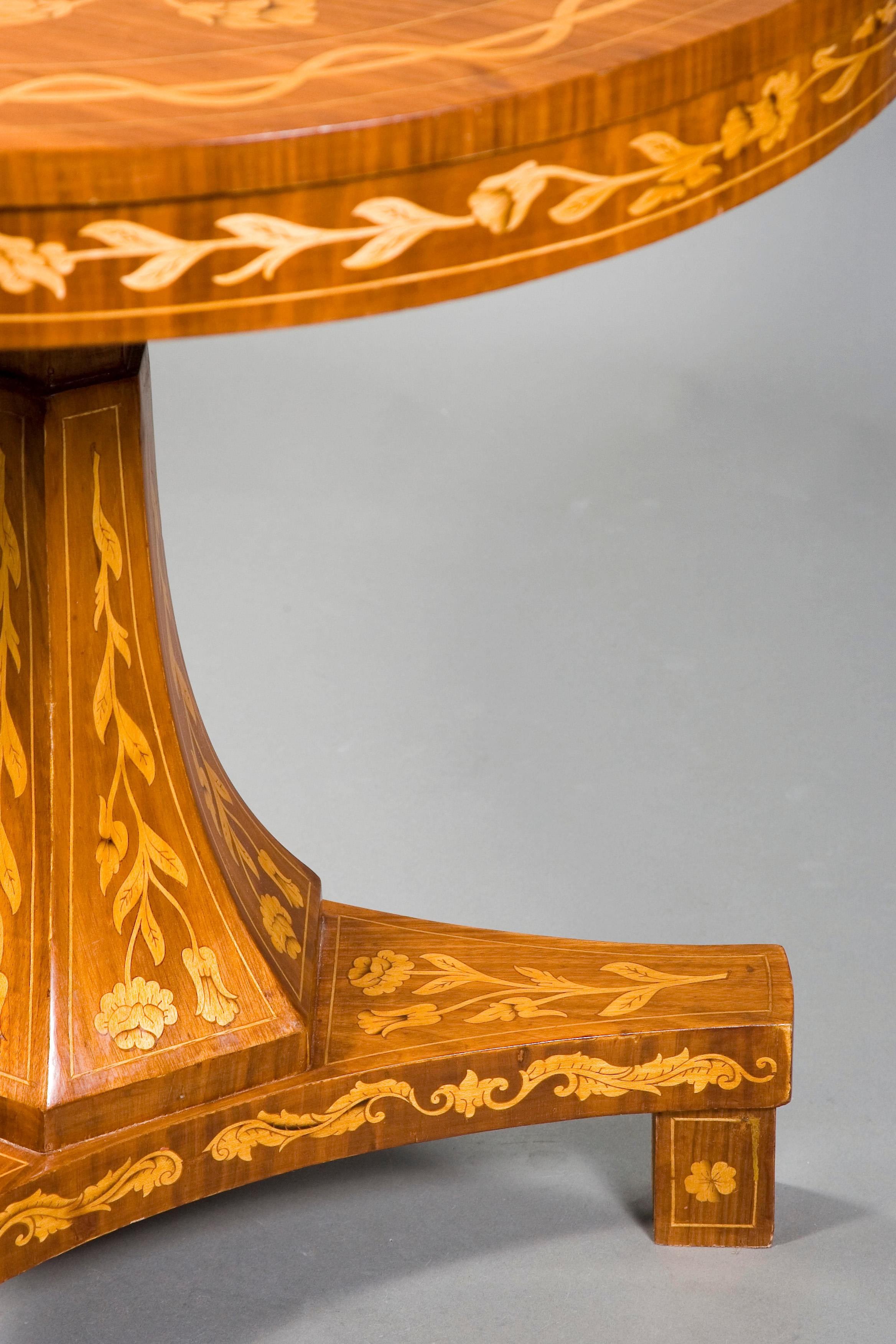 Cherrywood. 
Slightly protruding tabletop with cambered frame. Base plate drawn in on three sides on block feet. Column shaft ascending in the center, six times edged and stepped. Comprehensive inlaid decoration of leaf and blossom tendrils made of