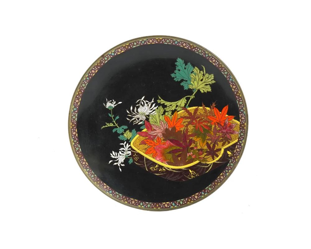 Assiette émaillée japonaise ancienne de haute qualité, datant de la fin de l'ère Meiji. L'intérieur de l'assiette est orné d'une image en émail polychrome d'une caisse avec des feuilles d'automne et des fleurs de Chrusantemum sur le fond noir,