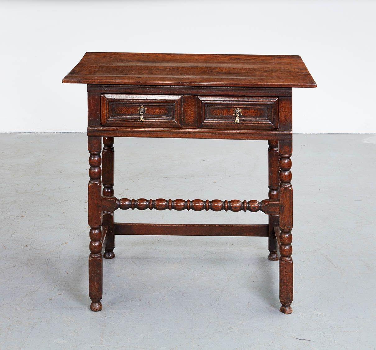 An English oak side table with pegged top over single drawer with dual bevelled front panels each with drop pull, over bobbin turned legs joined by square section stretchers to back and side, and high egg and dart turned stretcher to front, on