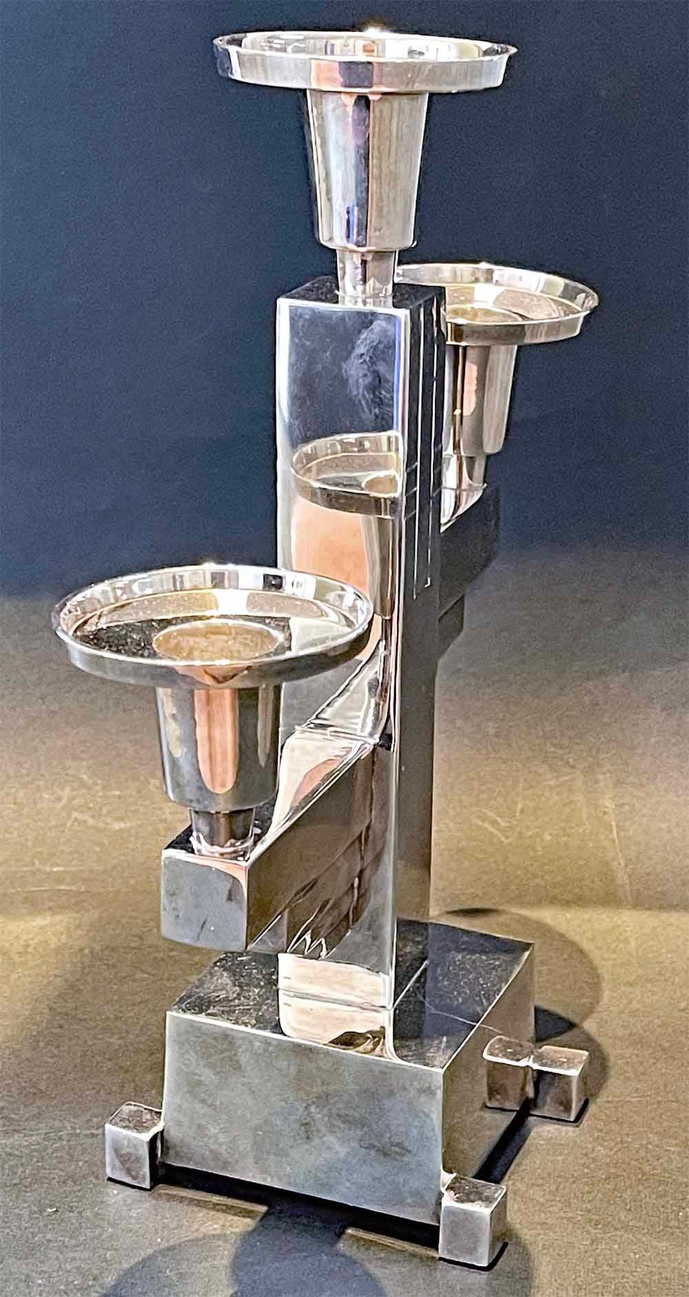 Dieser seltene und auffällige Kandelaber im High Style Deco verfügt über drei Kerzenfüße, von denen einer oben auf einem Pfosten mit eingeschnittenen geometrischen Verzierungen sitzt, während die beiden unteren auf vorspringenden horizontalen Stäben