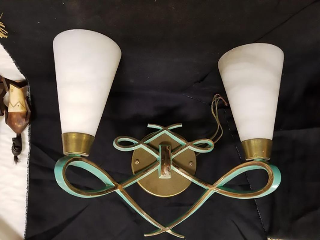 French Art Deco style wall sconce pair in the style of designer Jules Leleu. This pair of wall sconces have been cast in bronze with brass shade holders. Elegant scroll or ribbon patterns each with a uniquely beautiful dual color design hi-polished
