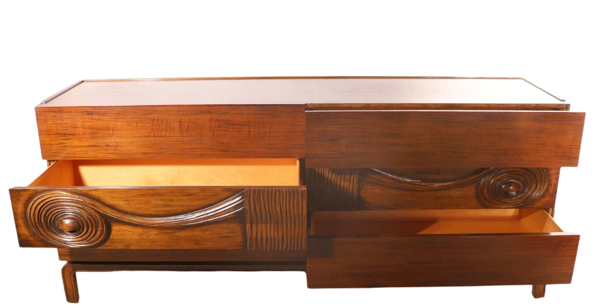 Voguish dresser designed by Edmond Spence, made in Sweden, ca. 1950/1960's. The dresser features six deep drawers, the middle drawers having  deeply carved fronts with a  dramatic swirl motif. The case is constructed of vibrant Macassar veneer, on