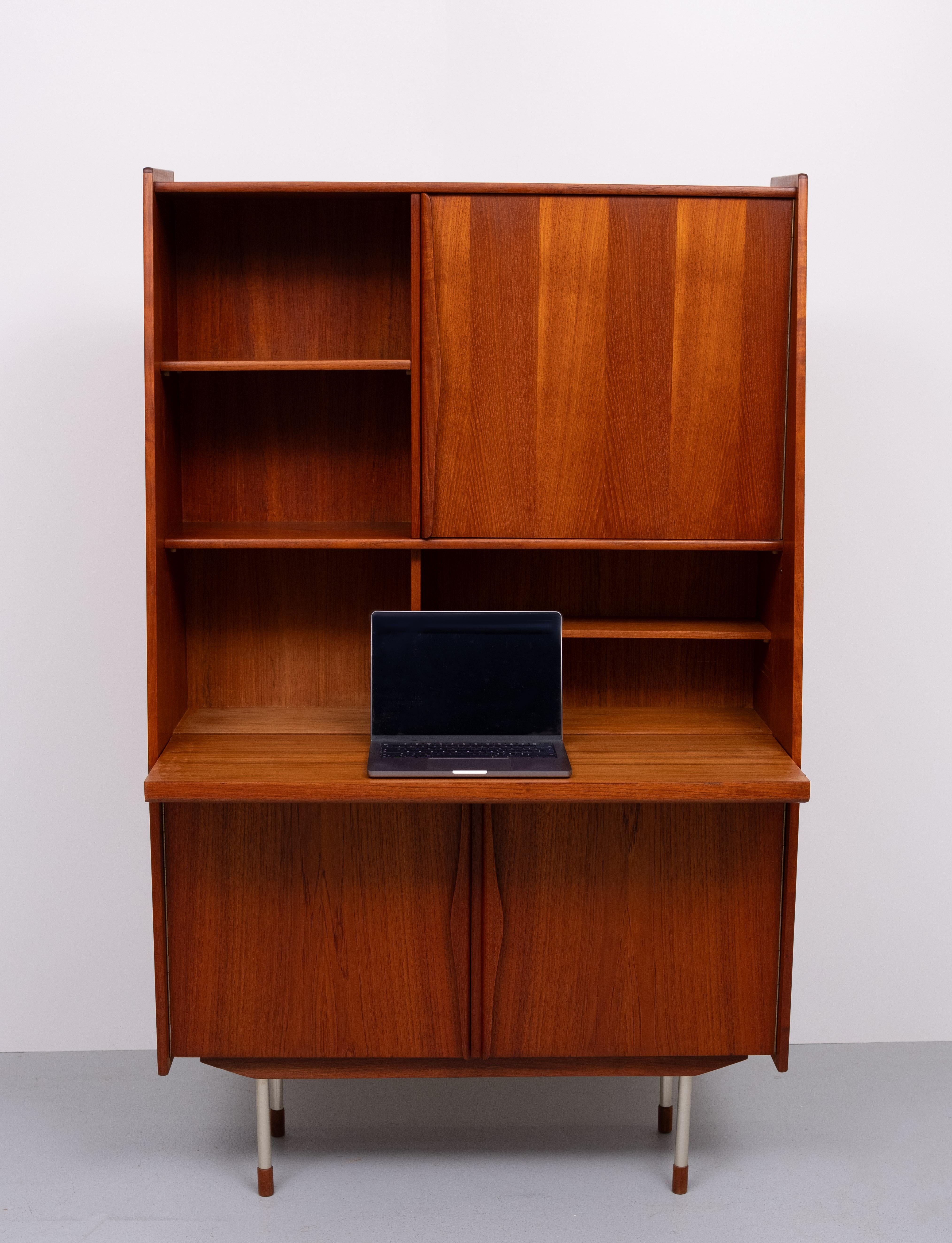   
Questa bellissima segretaria in teak è stata realizzata negli anni '60.   
Maniglie dalla forma organica molto bella. Gambe in alluminio con estremità in teak.
ha un piano estraibile da utilizzare come comoda scrivania. In basso dietro le porte a