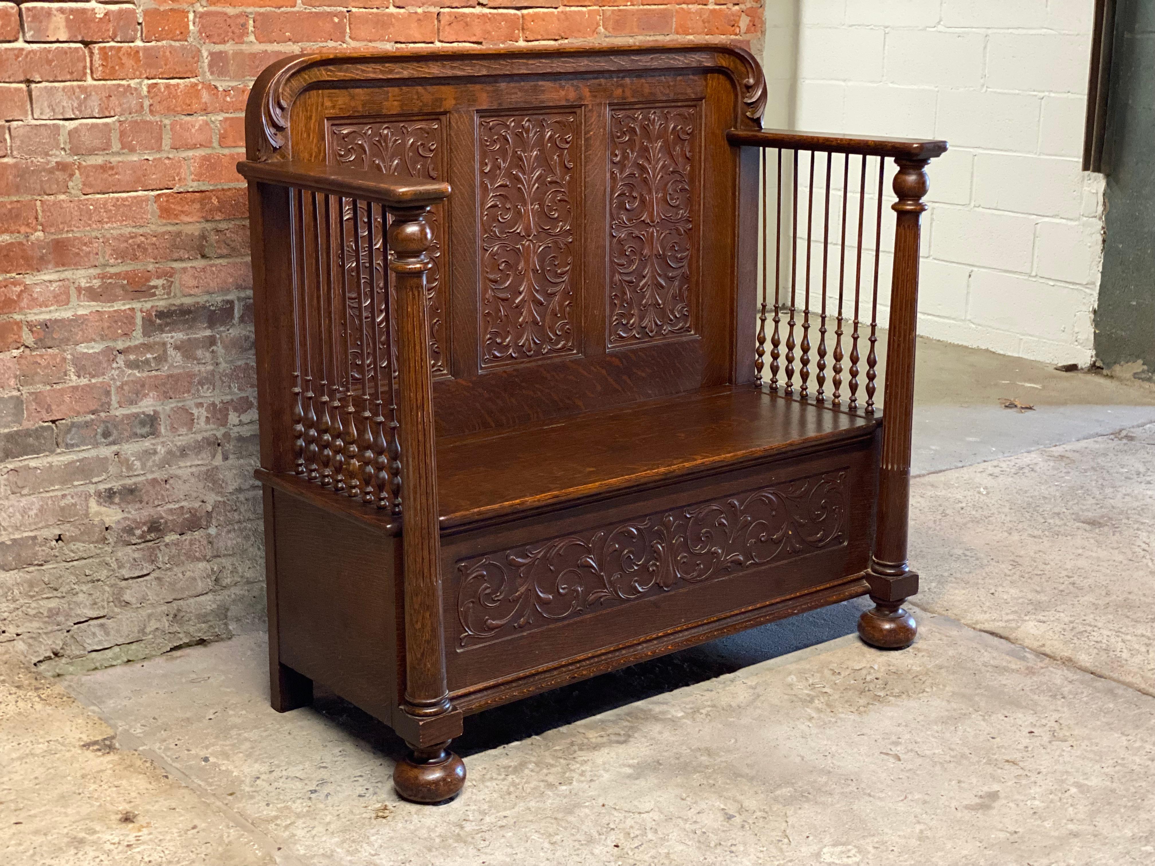 Amazing Victorian quarter sawn and carved oak deacon's bench with roomy under seat storage. Featuring carved leaf and scroll relief recessed panels with high paddle arms, spindle gallery sides, fluted columns and bun feet. Circa 1870-1890.