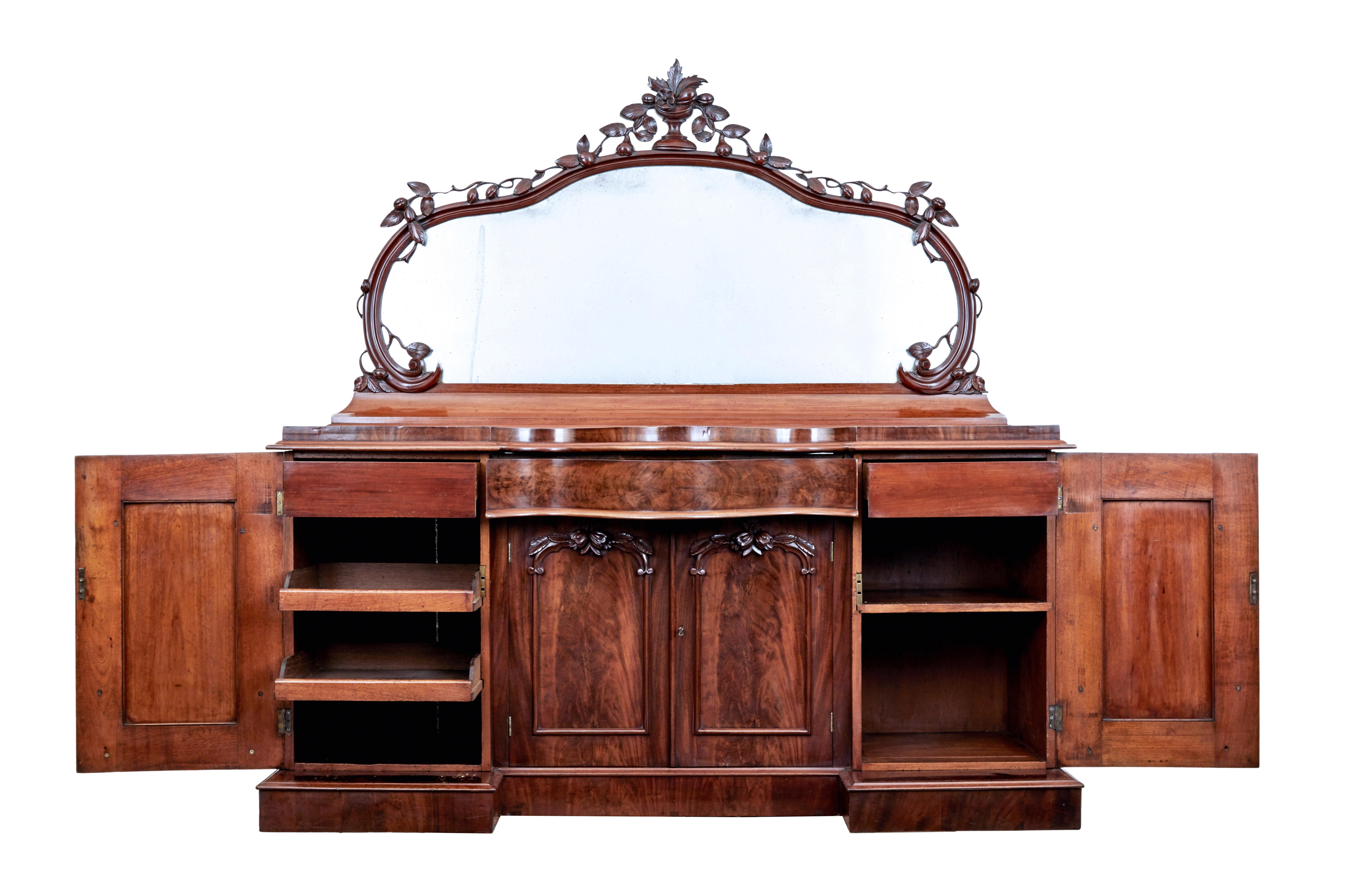 High Victorian shaped flame mahogany mirror topped sideboard circa 1860.

Fine quality 2 part sideboard. Shaped mirror with original plate, carved cup at the top with flowing leaves and fruit flowing down to the scrolled base of the