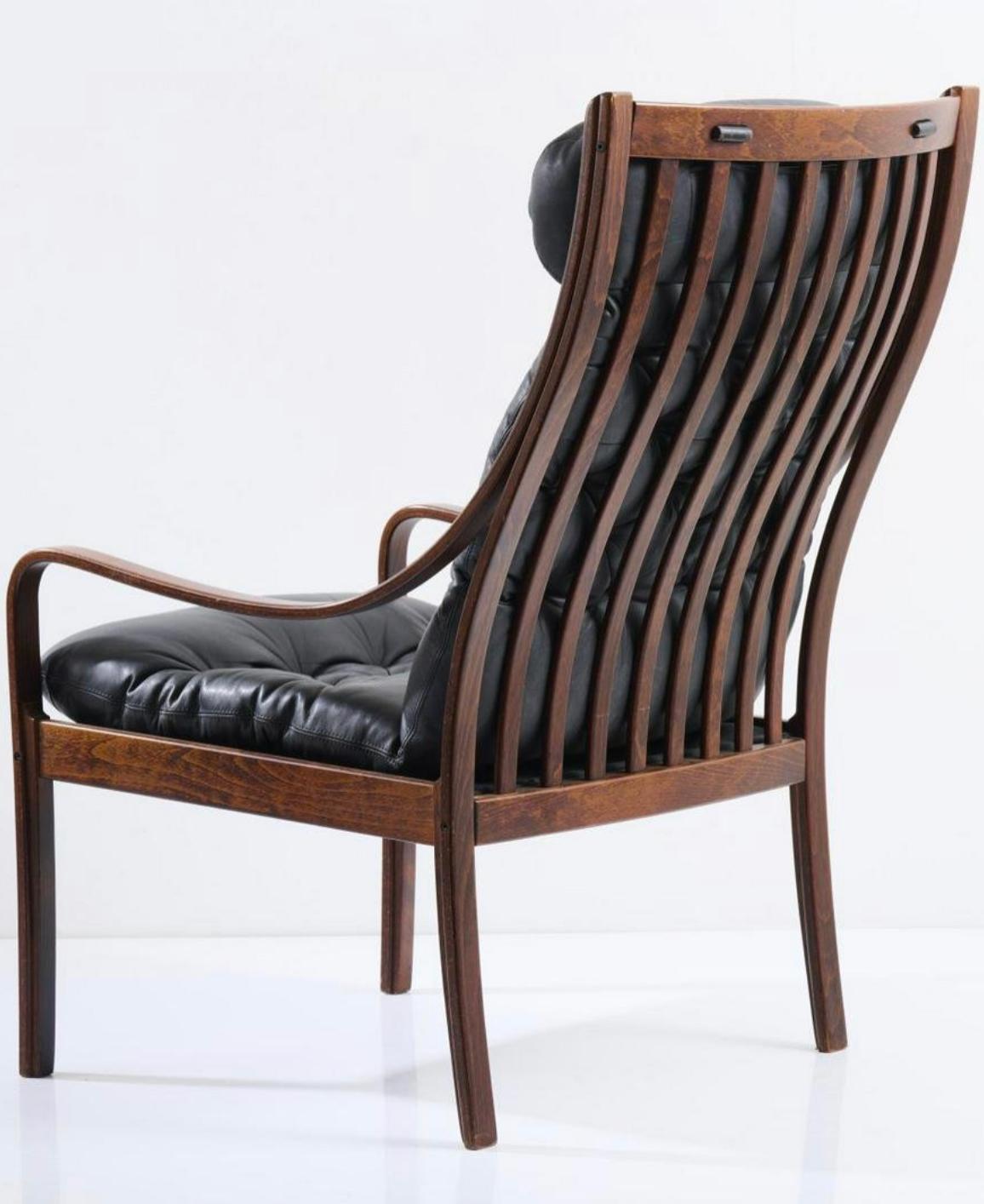 Experience the epitome of mid-century modern design with this stunning Fredrik A. Kayser armchair, produced by Vatne Möbler in the early 1960s. The highback armchair features a black leather upholstery and a stained elmwood frame, creating a