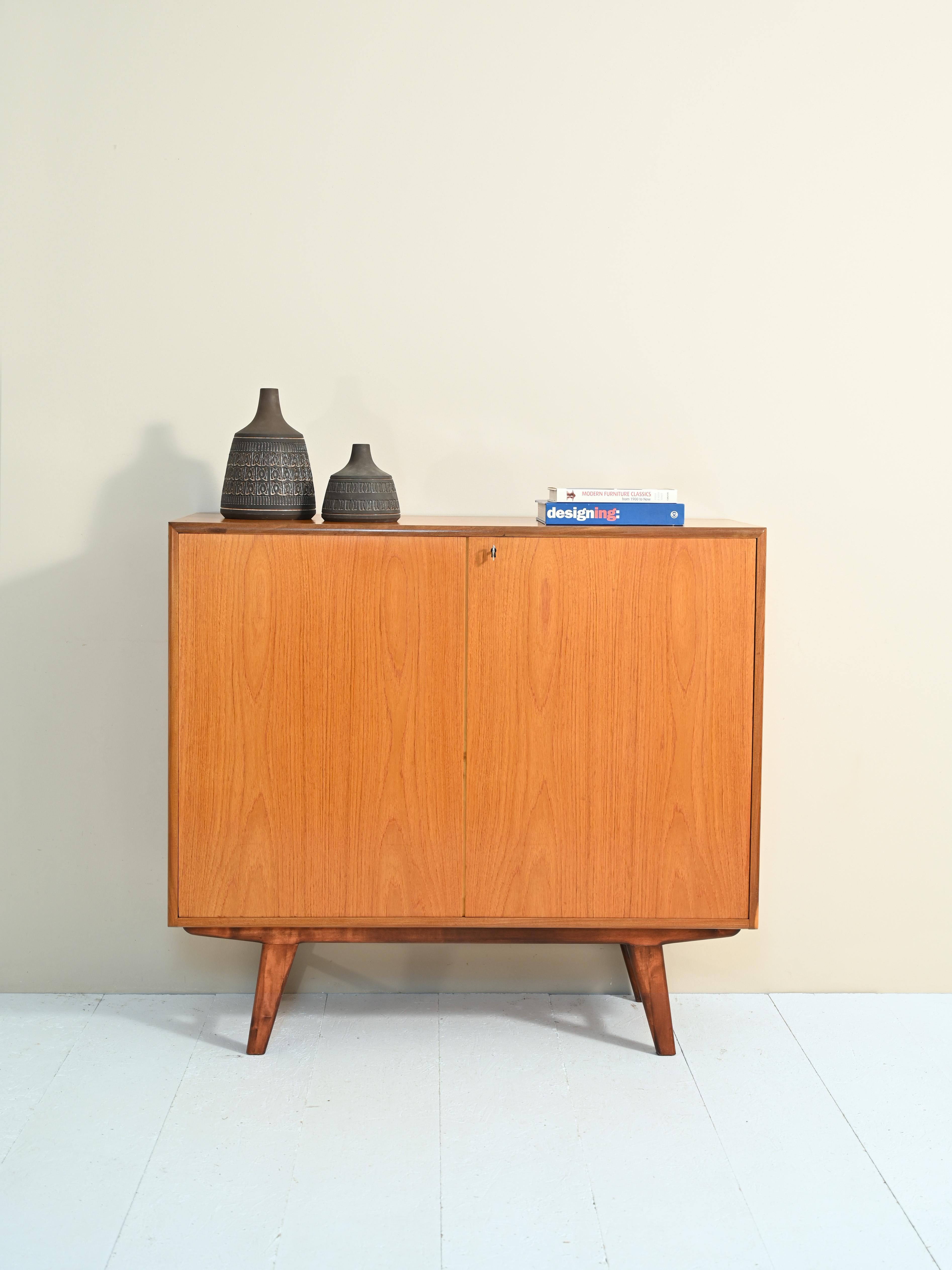 Scandinavian cabinet from the 1950s/60s made of teak.

Vintage sideboard with hinged doors, inside hides three drawers and three very capacious compartments.

The tapered games and the frame on which they rest give lightness to the