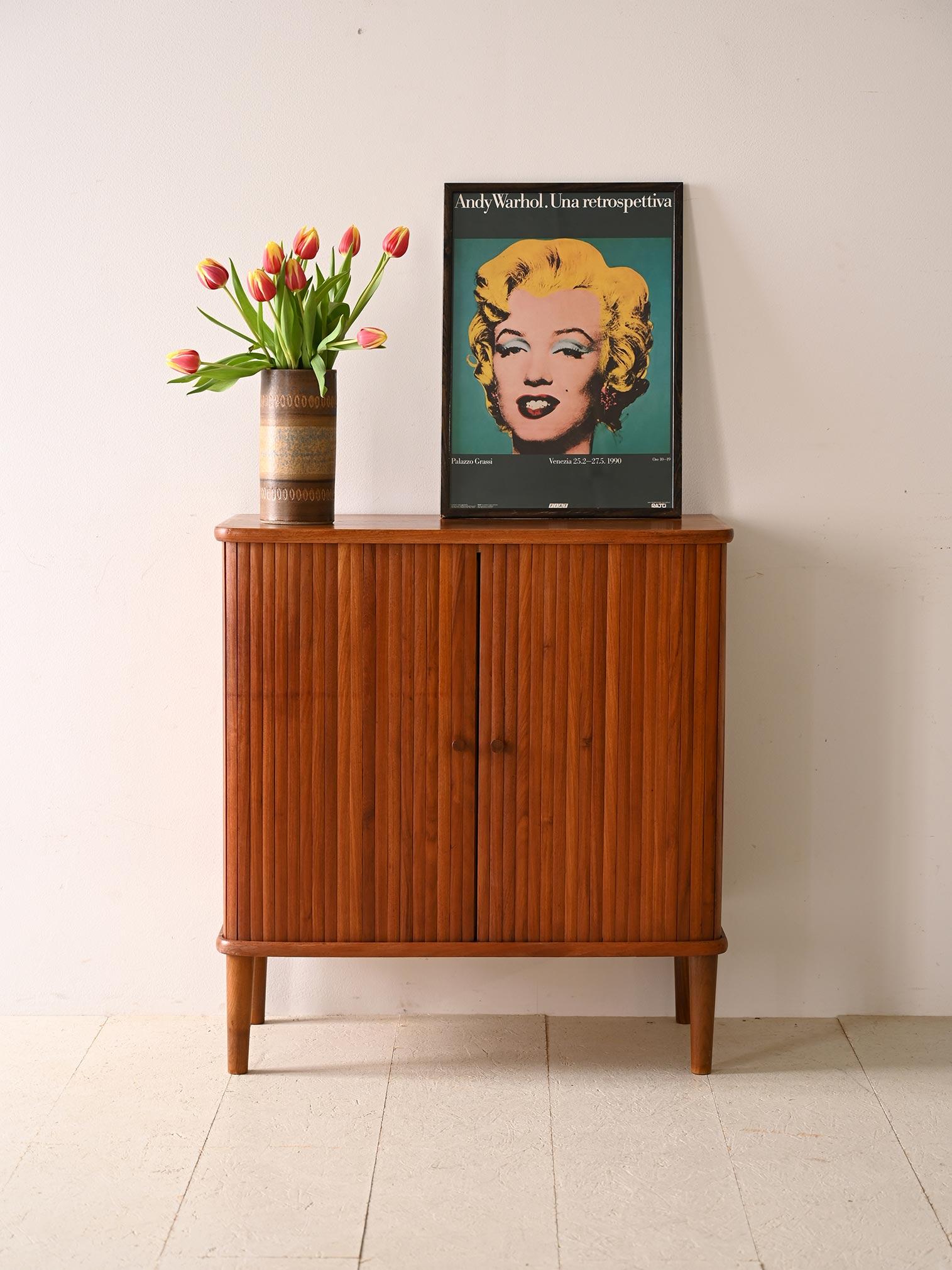 Vintage teak cabinet with hinged doors. An original piece of furniture with classic and elegant shapes. The figure features soft lines and rounded corners; the distinctive doors are formed from teak wood strips. The small door knobs and the bold