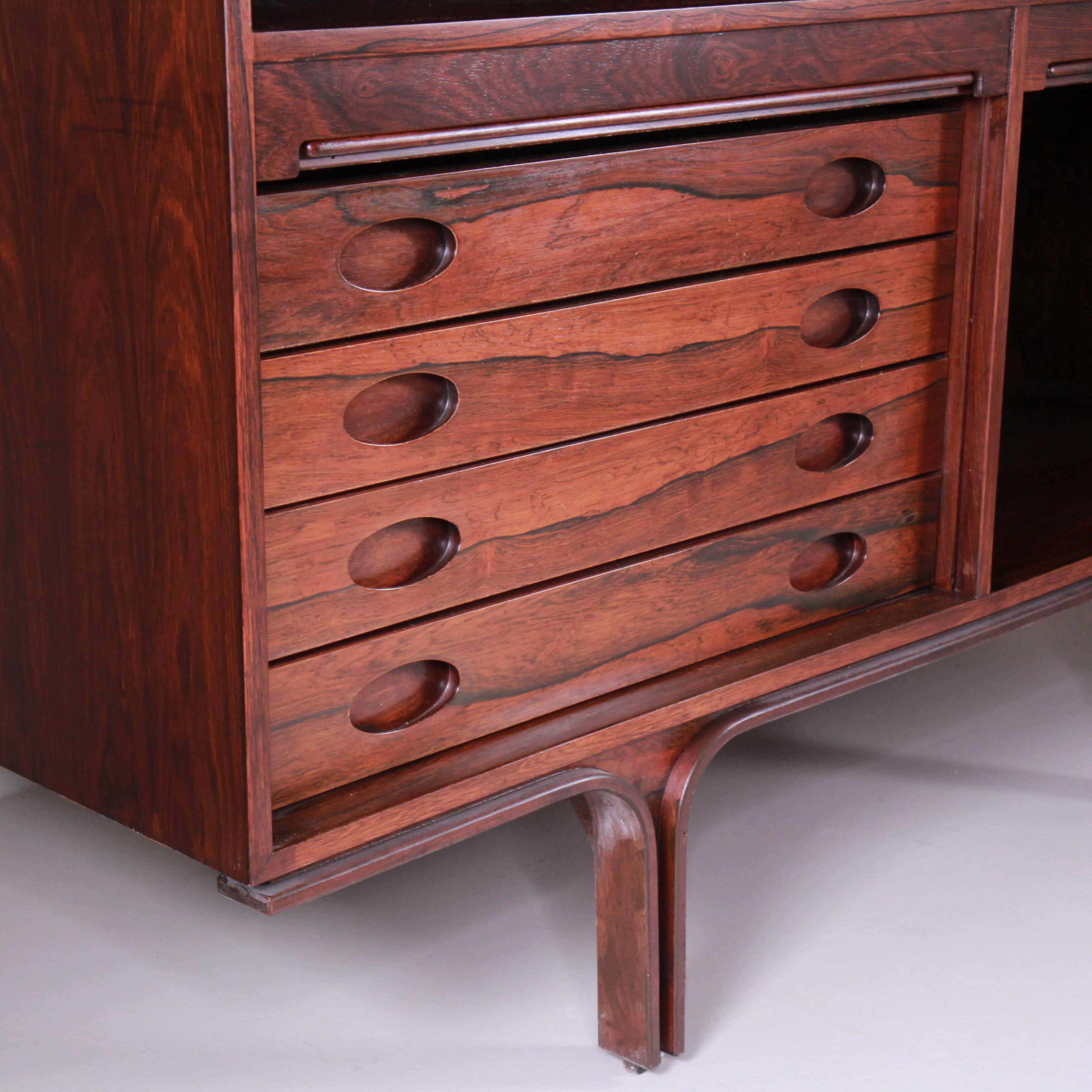 L’Highboard modello 504 di Gianfranco Frattini, prodotto da Bernini nel 1960, è un mobile che combina l’eleganza del legno di palissandro con un design funzionale e raffinato. Il pezzo è caratterizzato da serrandine in legno che scorrono dolcemente