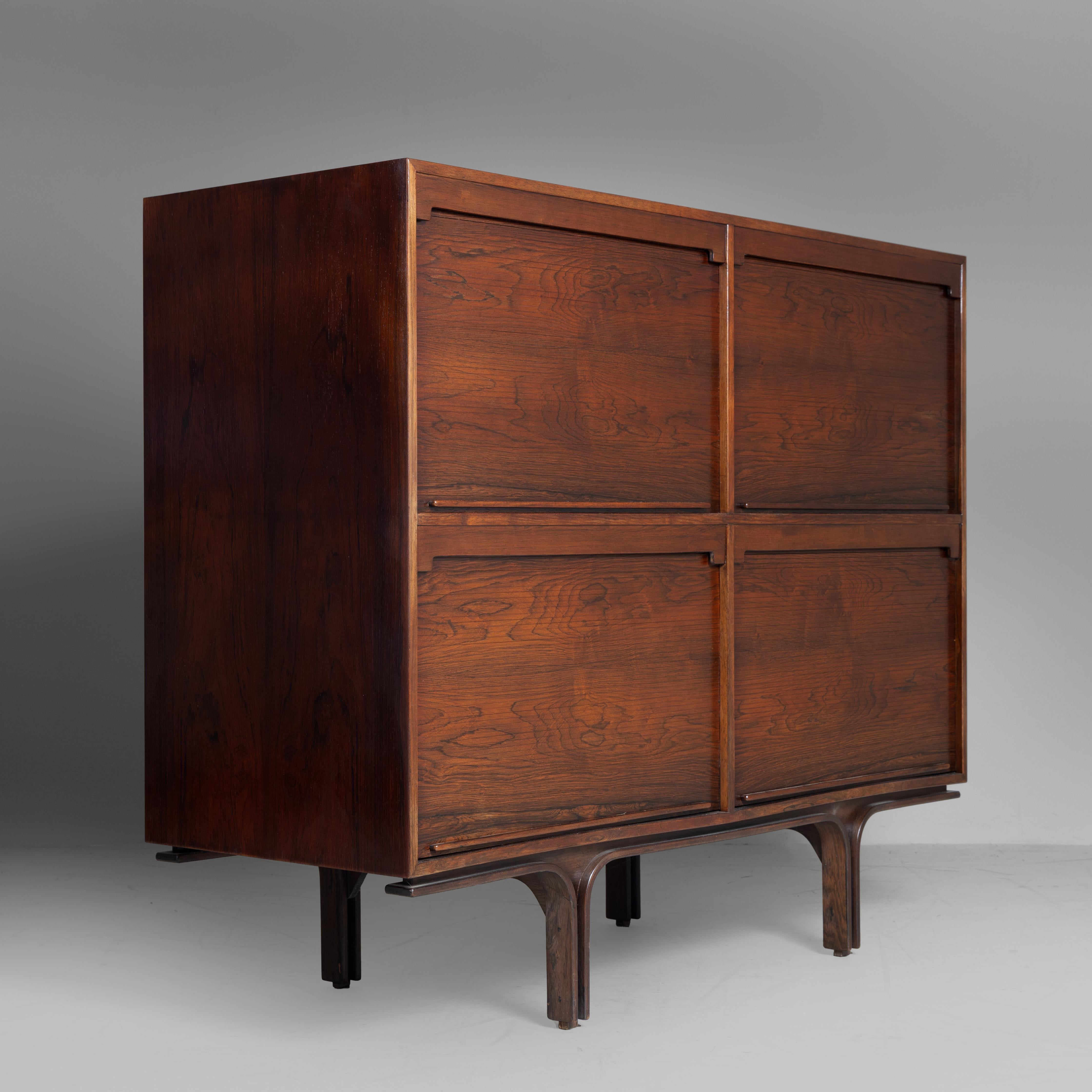 Das Highboard Modell 504 von Gianfranco Frattini, das 1960 von Bernini hergestellt wurde, ist ein Möbelstück, das die Eleganz von Palisanderholz mit einem funktionalen und raffinierten Design verbindet. Die hölzernen Fensterläden lassen sich