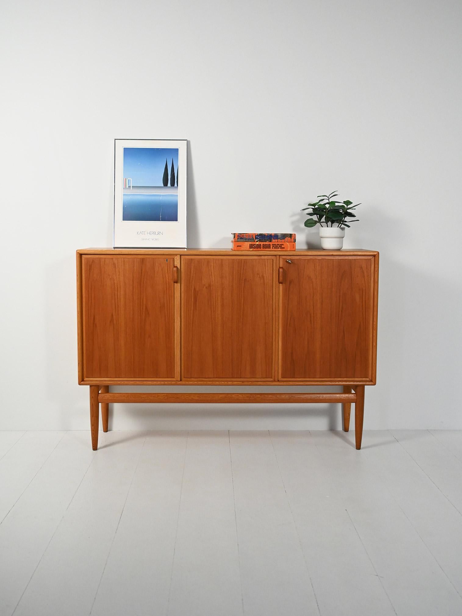 Highboard con struttura in rovere e ante in teak fiammato. Tre ante con maniglie in rovere curvato, linee leggere.

Highboard con struttura in rovere dal profilo arioso con gambe affusolate e maniglie in rovere curvato a vapore, cifra del design
