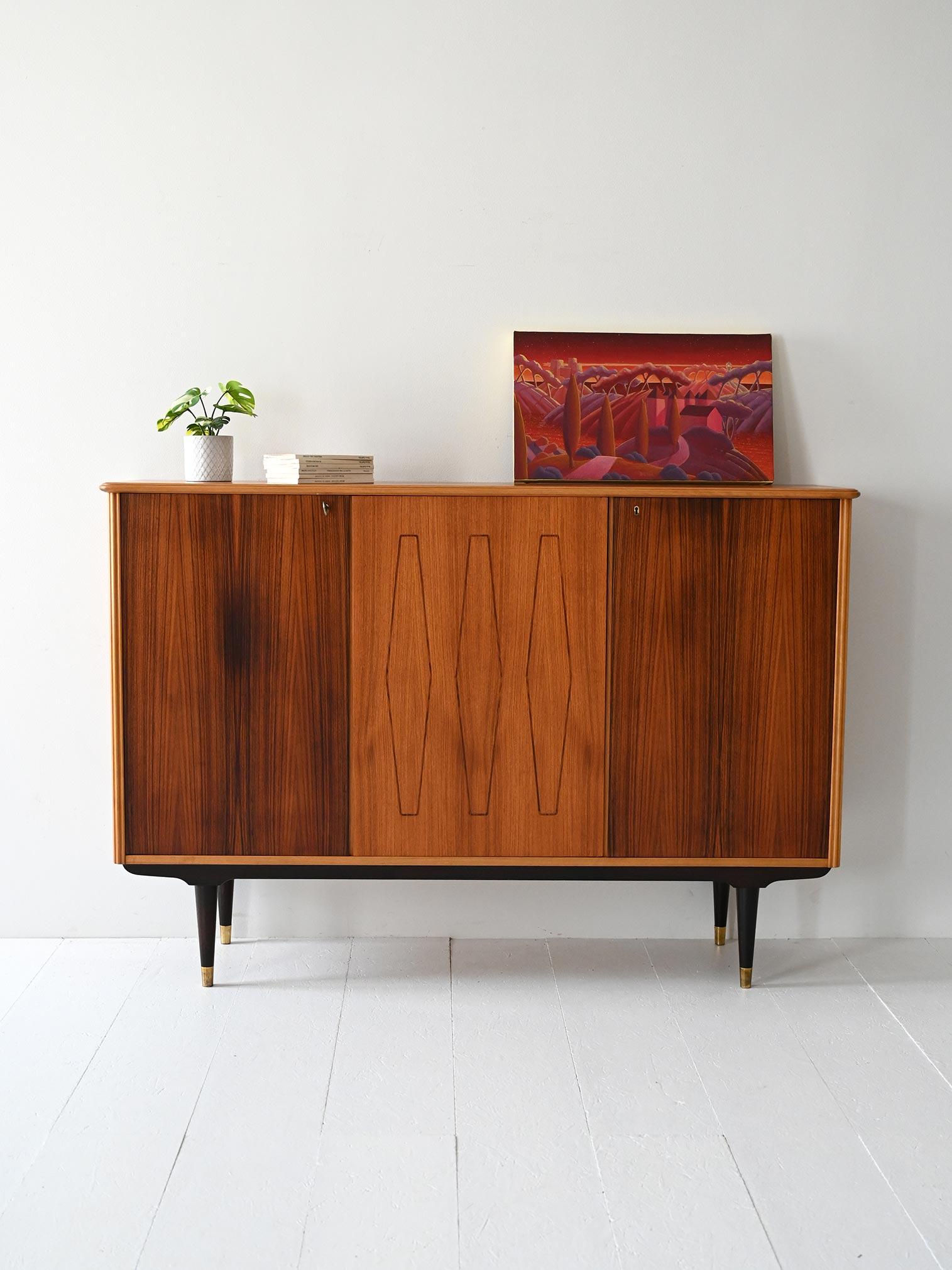 Tall 1950s cabinet with graphic grain, contrasting inserts, and elegant brass details. Mid-century Nordic style.

Scandinavian 1950s teak highboard with graphic grain and contrasting light-colored inserts. The darker, turned legs are finished with