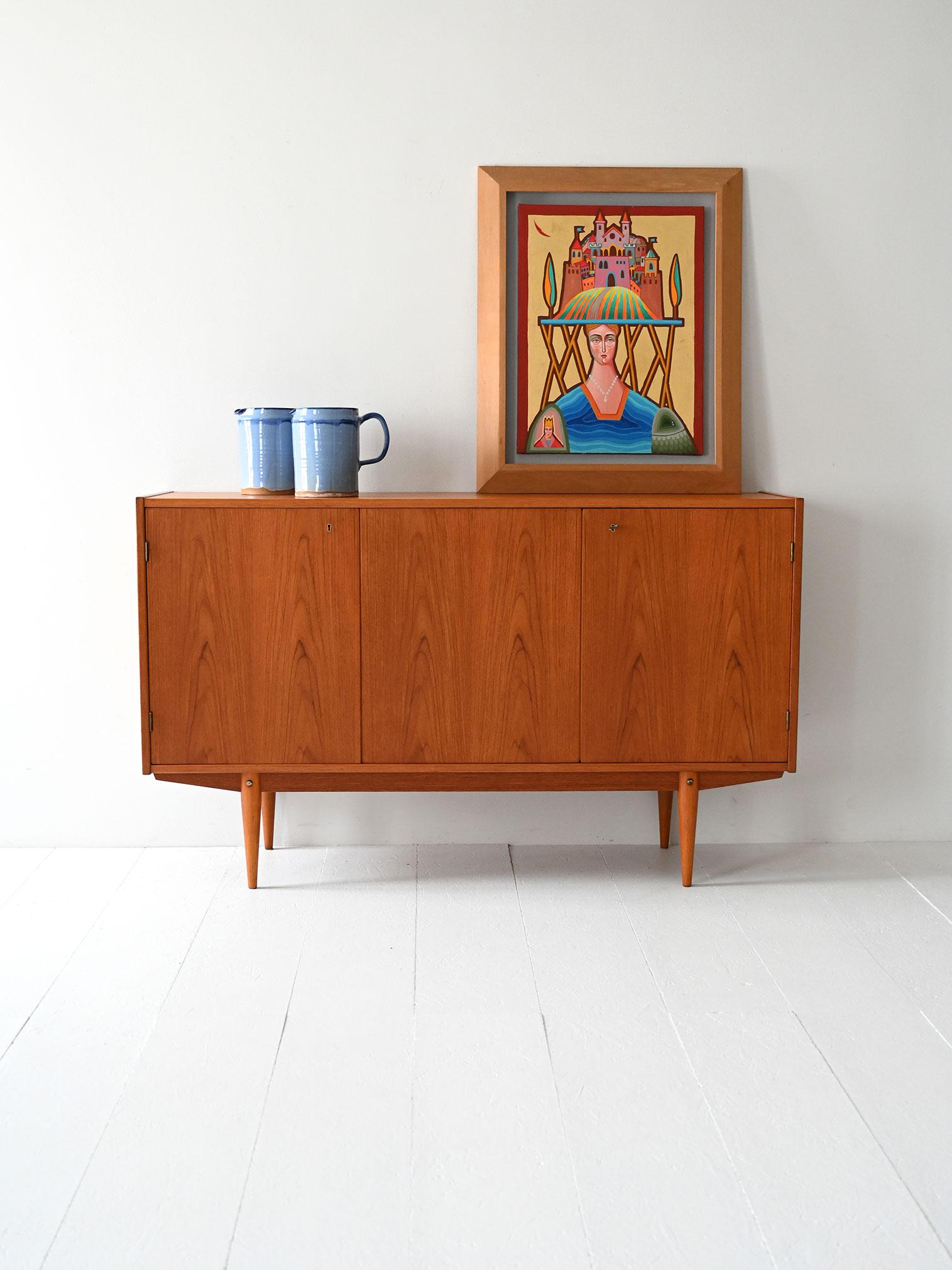 Vintage three-door teak cabinet with interior shelves and drawers. Understated, elegant and functional lines.

Scandinavian 1960s highboard with triple teak hinged door. The interior is organized with two compartments: one with two shelves, the