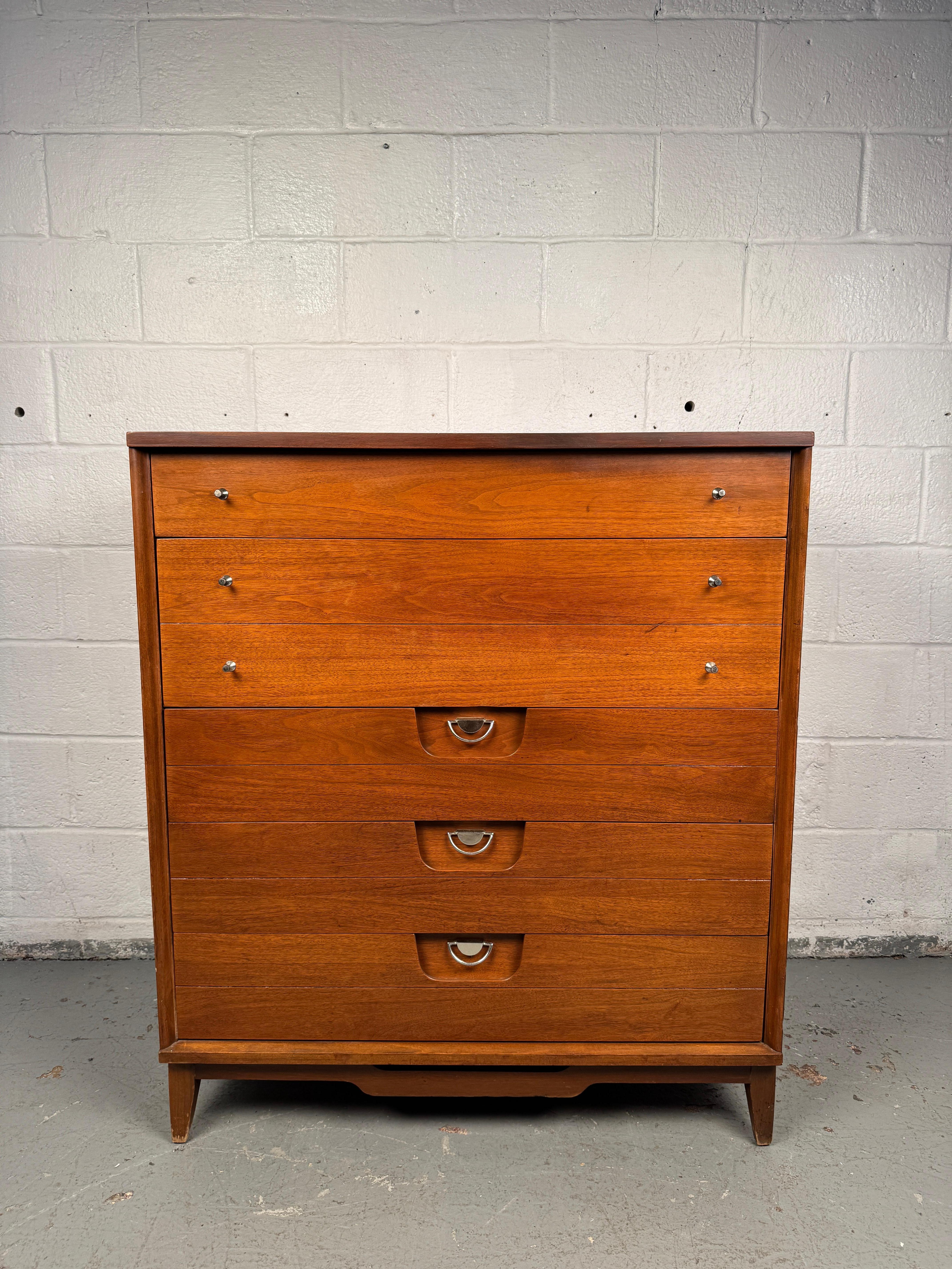 Handsome mid-century highboy dresser manufactured by Basic Witz, crafted in warm walnut. Features a unique sculptural facade with distinctive integrated handles, combining bold design with practical storage. A striking example of American