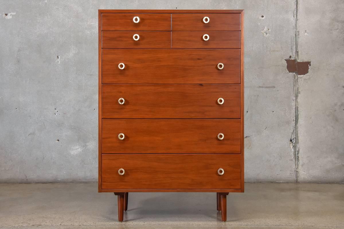An uncommon highboy dresser designed by Greta Grossman for Glenn of California. With four large lower drawers and four small upper drawers this piece offers a ton of storage. The signature round brass pulls are a beautiful accent against the walnut