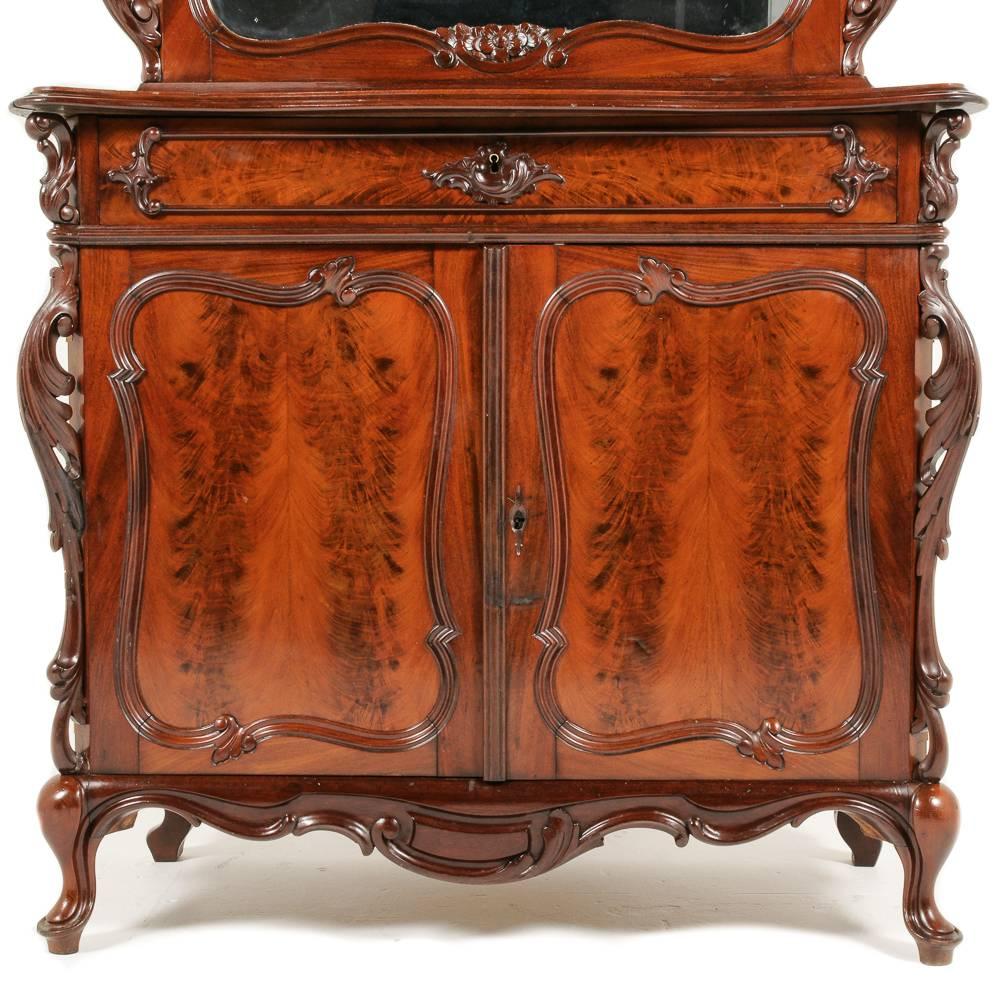 A highly-carved Continental Victorian cabinet, with elaborate pierced carving to the top and sides, the top with a mirrored door, and with dramatic veneer door and drawer fronts below, circa 1860.



 