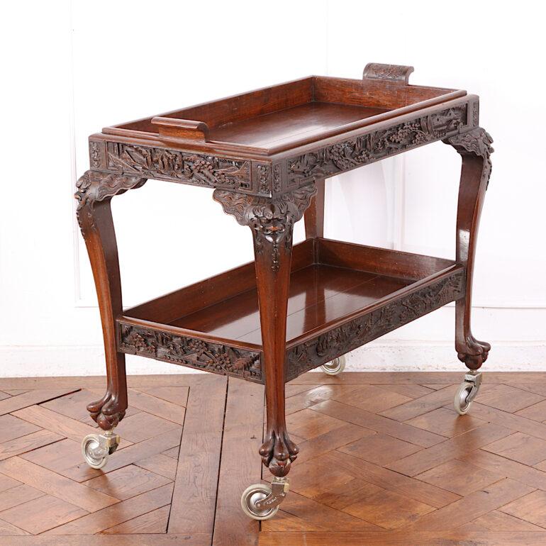 A highly-carved solid teak two-tier Asian trolley with removeable top tray, the elegant cabriole legs embellished with carved faces, the gallery sides of each tier carved with detailed landscapes. C. 1950.

