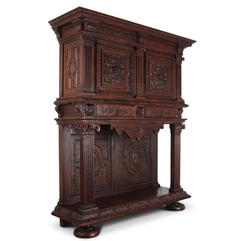 A highly-carved oak French Renaissance-Revival cabinet on stand, the two upper doors entirely covered with carved detailing and faces, and flanked by carved and fluted pilasters. Below the cabinet are two drawers, also embellished with carving, the